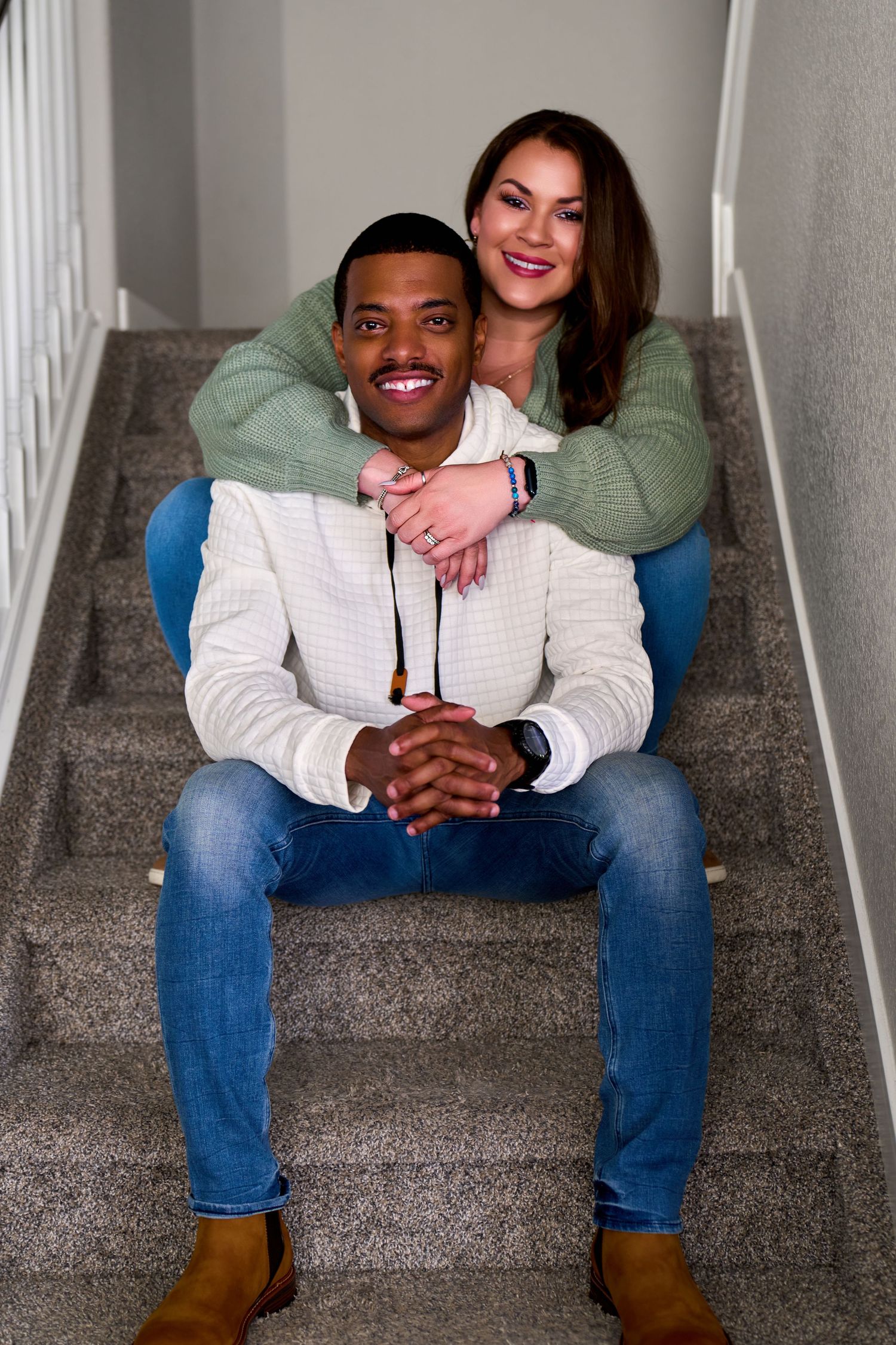 Happy couple sitting on carpeted stairs at home, sharing an intimate embrace while dressed in casual clothing.