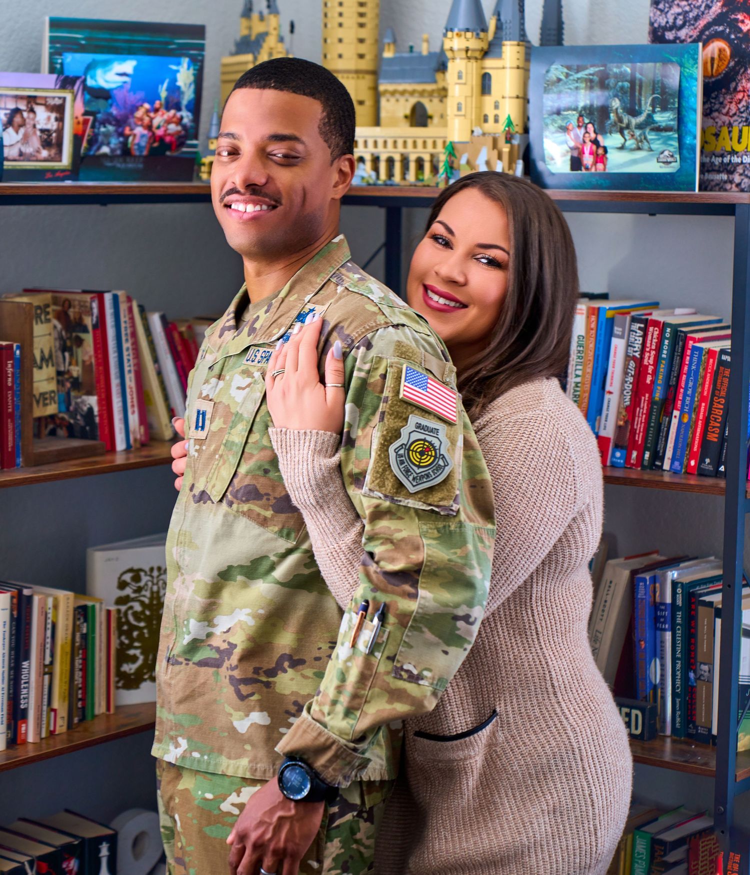 A couple poses together in front of a bookshelf with military and civilian books displayed behind them.