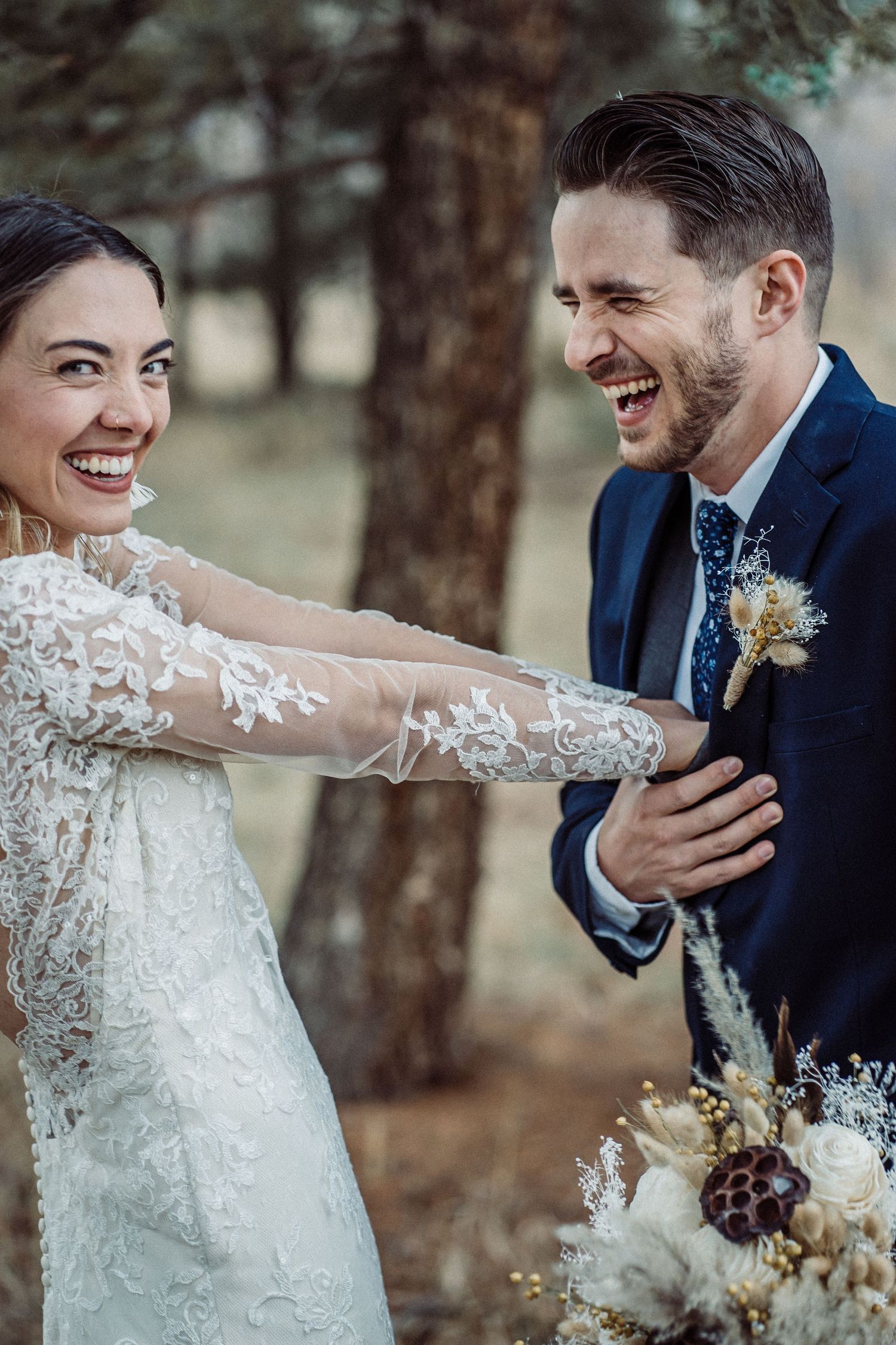 A joyful wedding couple sharing a candid laughing moment in their elegant attire with a bouquet.