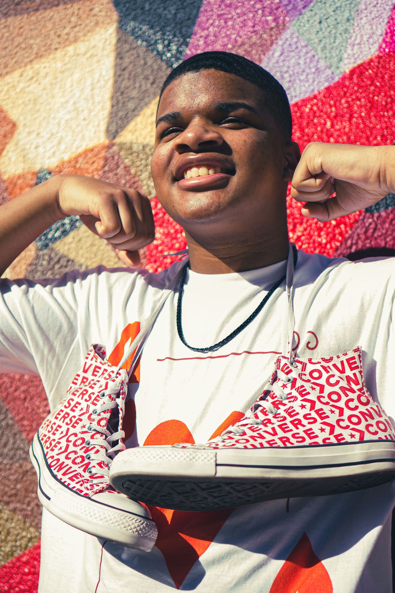 Person showing off red and white patterned sneakers against colorful wall background.
