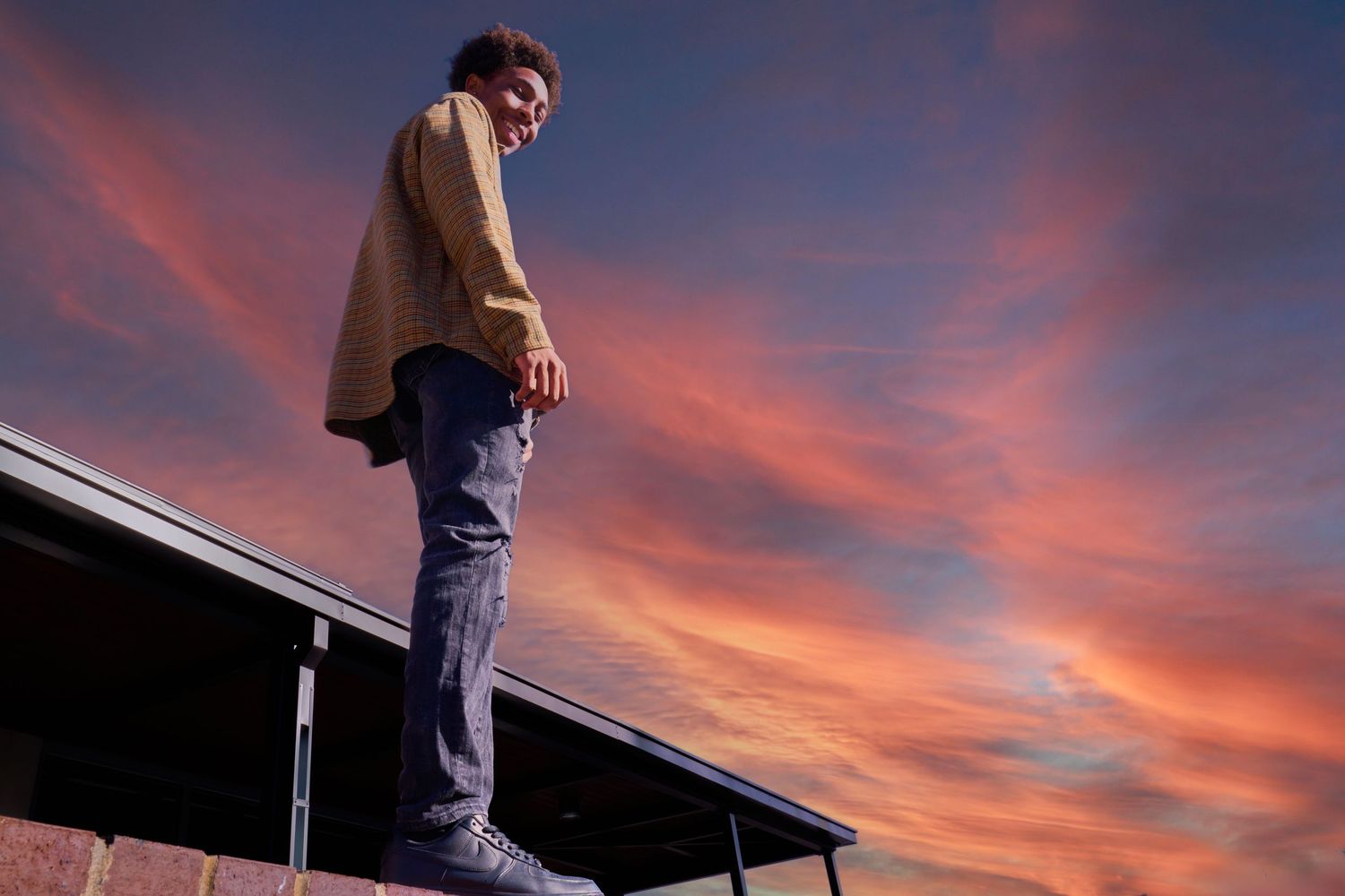 Silhouette of person standing on elevated surface against dramatic sunset sky.