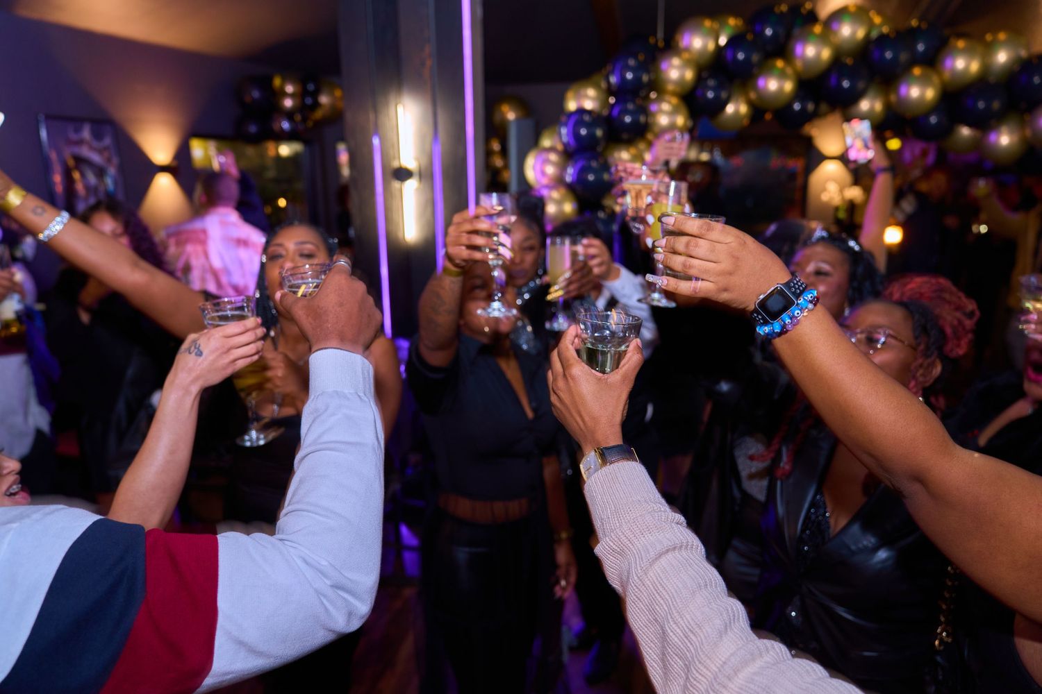 People raising glasses in celebration at nightclub with colorful lighting.