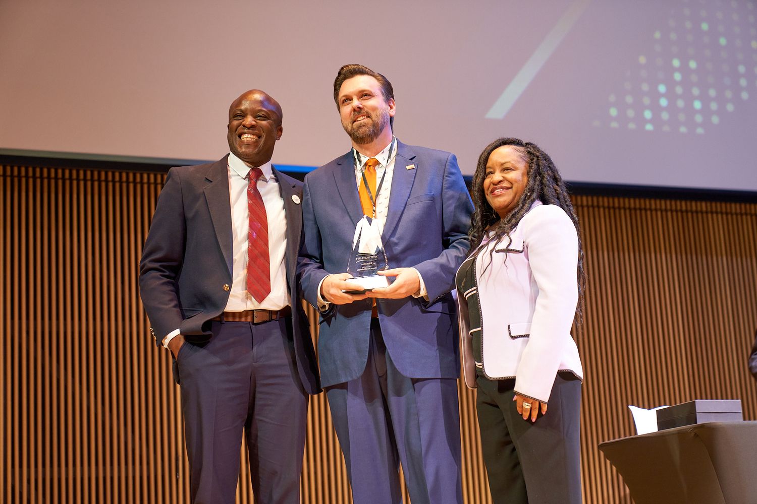 Three professionals on stage during an awards or recognition ceremony.