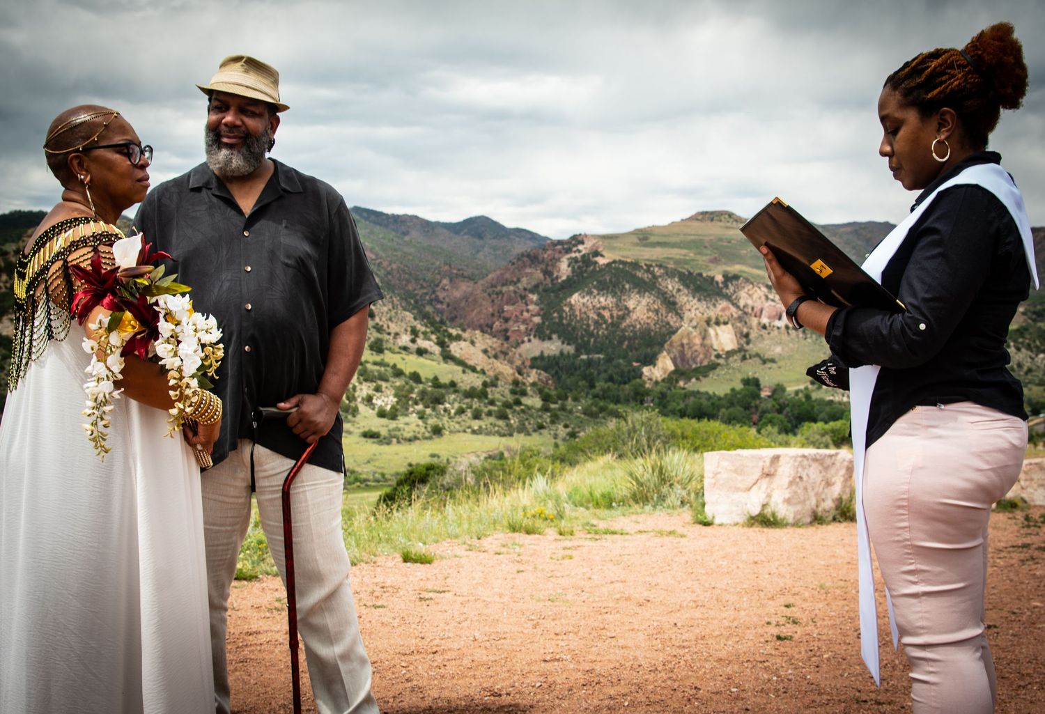 An outdoor wedding ceremony takes place against a scenic mountain backdrop.