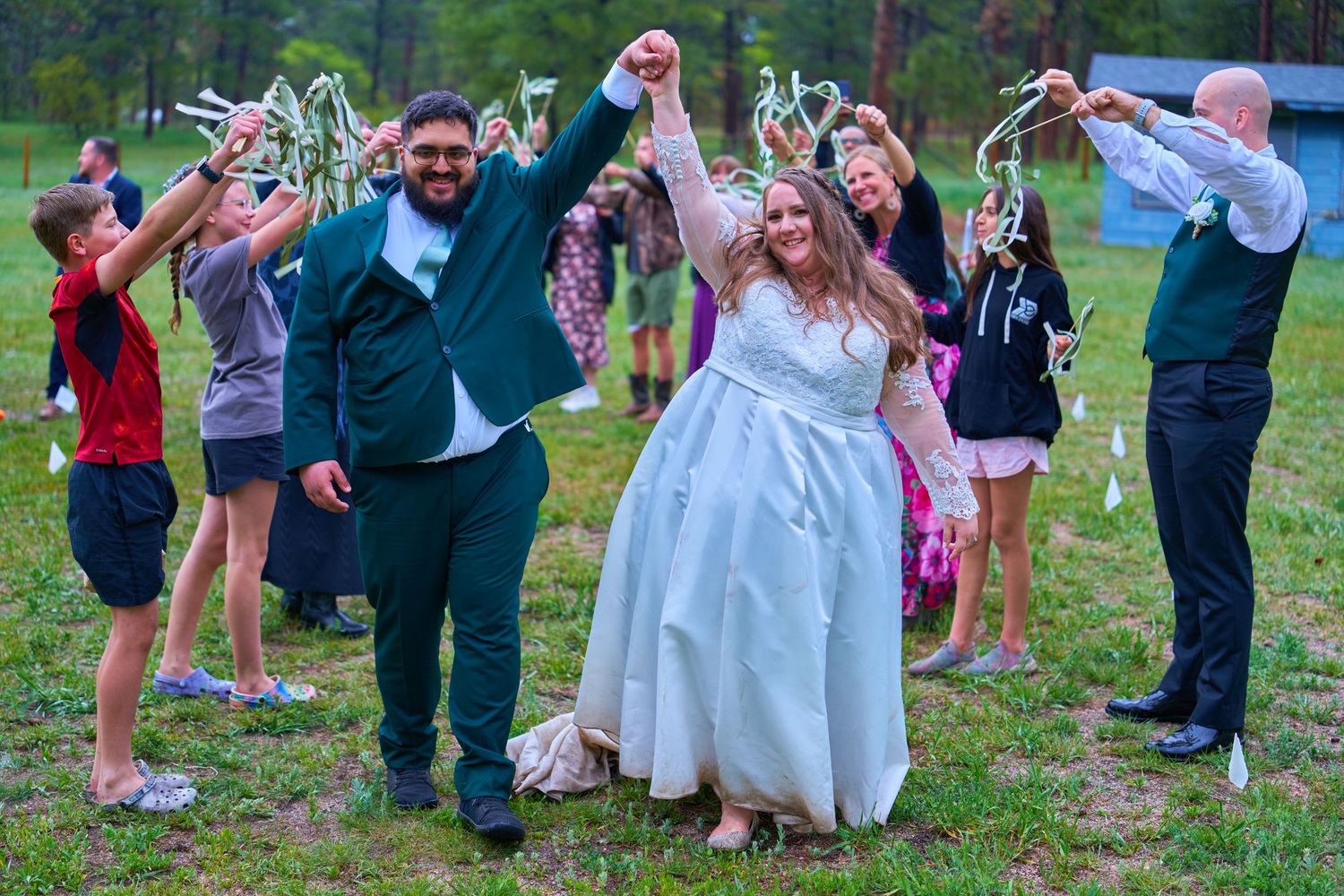 Wedding guests form celebratory arch for joyful newlyweds during outdoor reception.