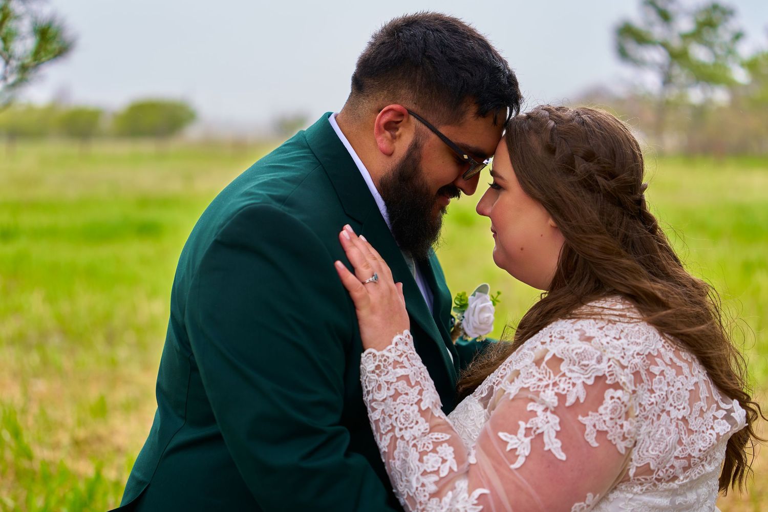 A romantic wedding moment captured outdoors with couple in emerald green suit and lace dress.