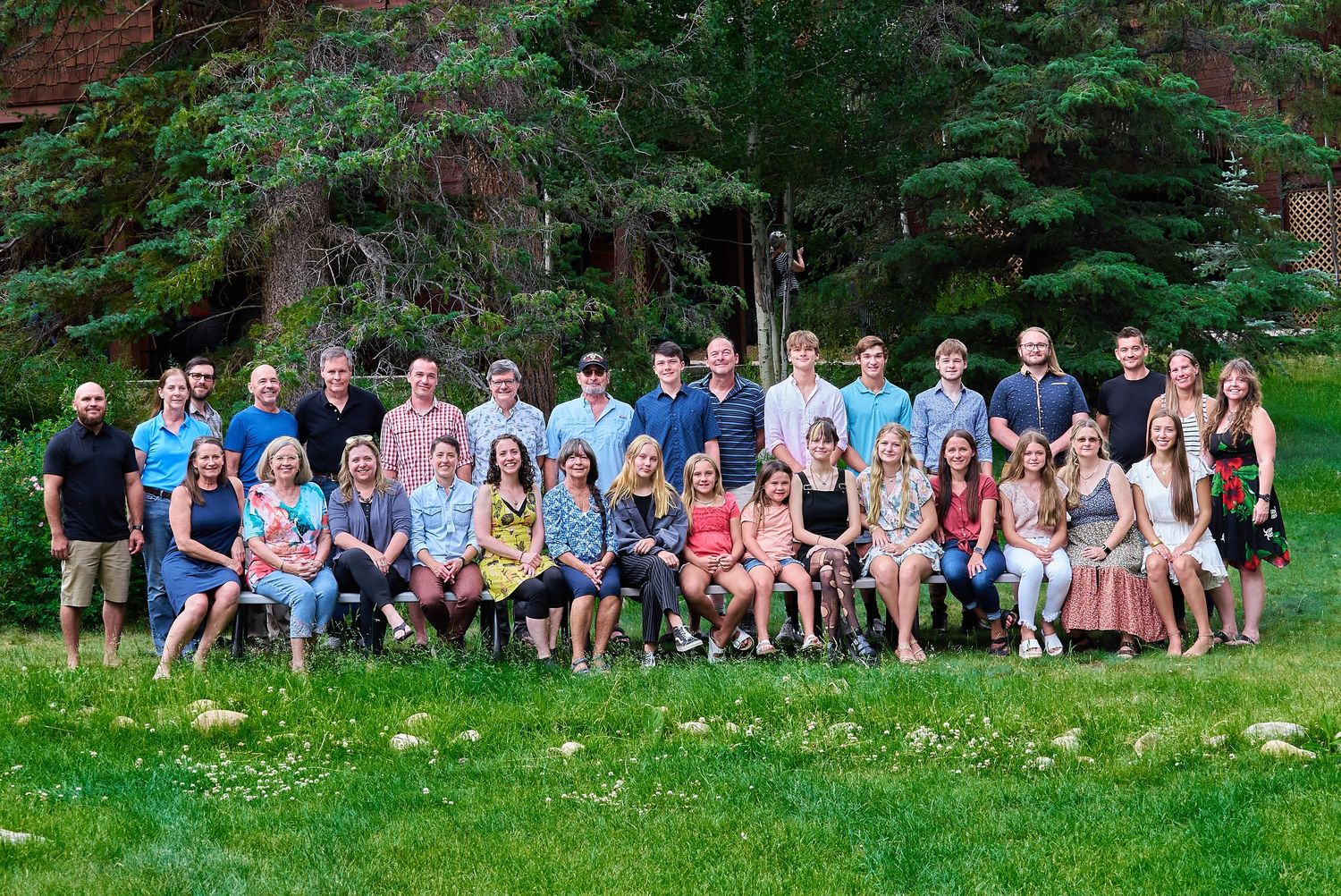 Large extended family group portrait outdoors on grass with trees and building in background.