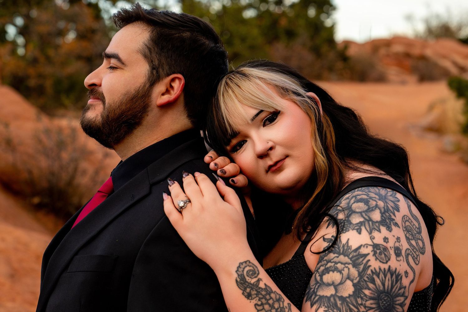 A couple embraces intimately in front of a desert landscape with red rock formations at sunset.