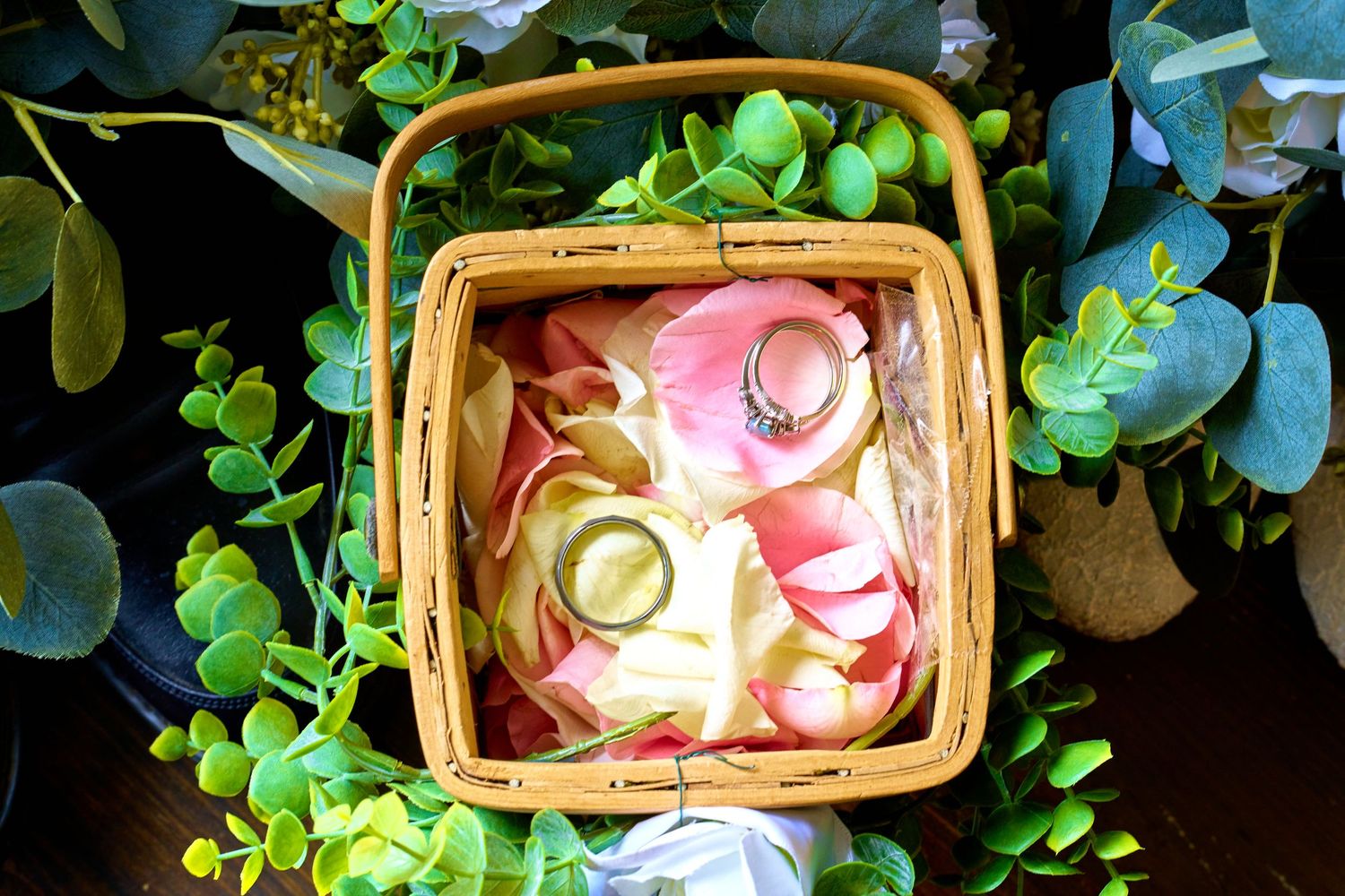Overhead view of pink and cream colored macarons in a woven bamboo basket surrounded by green succulent plants.