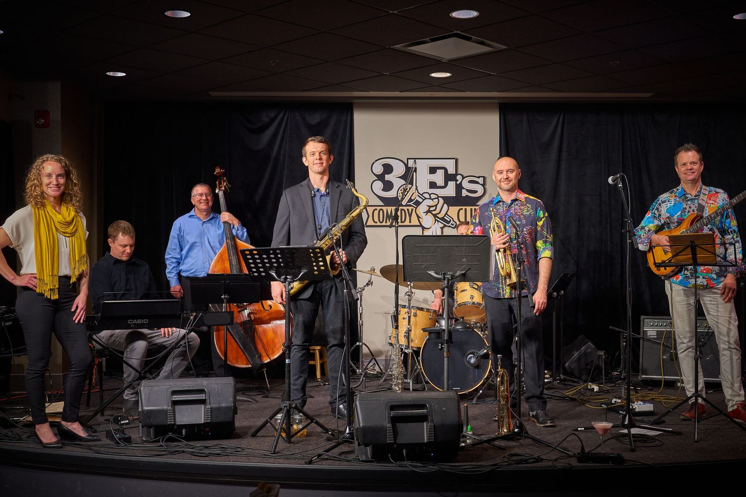 A live band performs on stage with various instruments including drums, bass, and guitar.