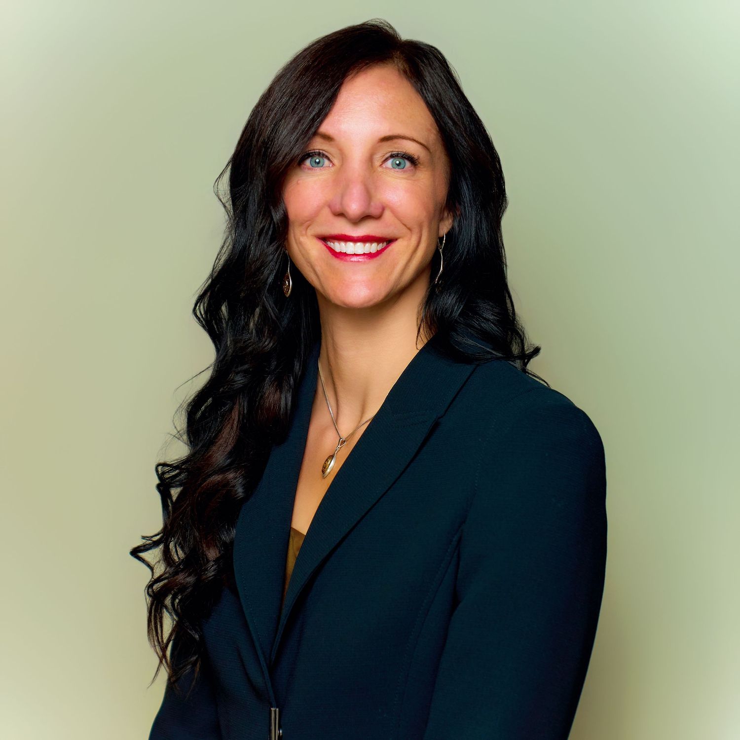 Professional headshot of a woman in a navy blazer with long dark hair against a light background.