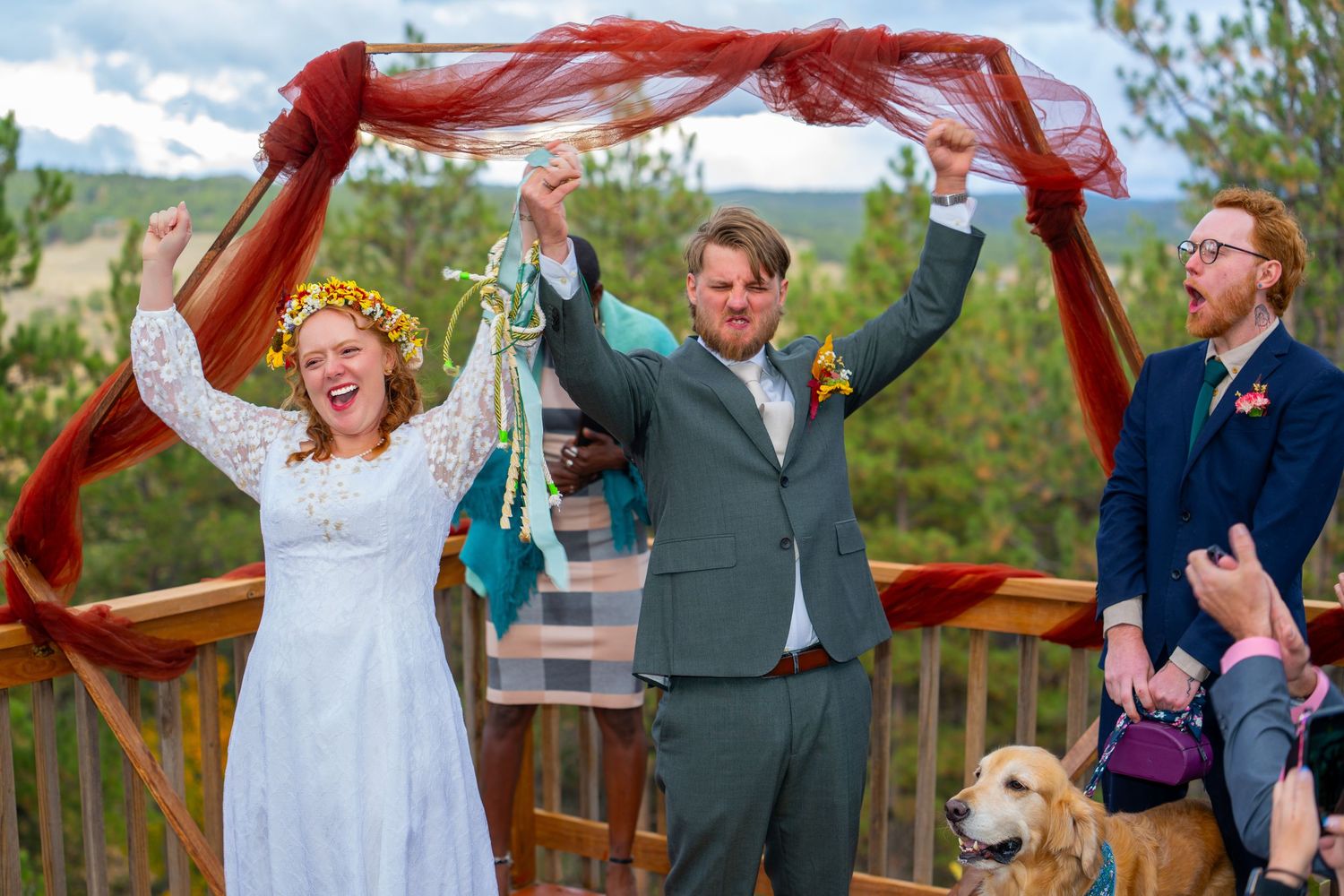 A joyful wedding celebration outdoors with a golden retriever dog on a wooden deck.
