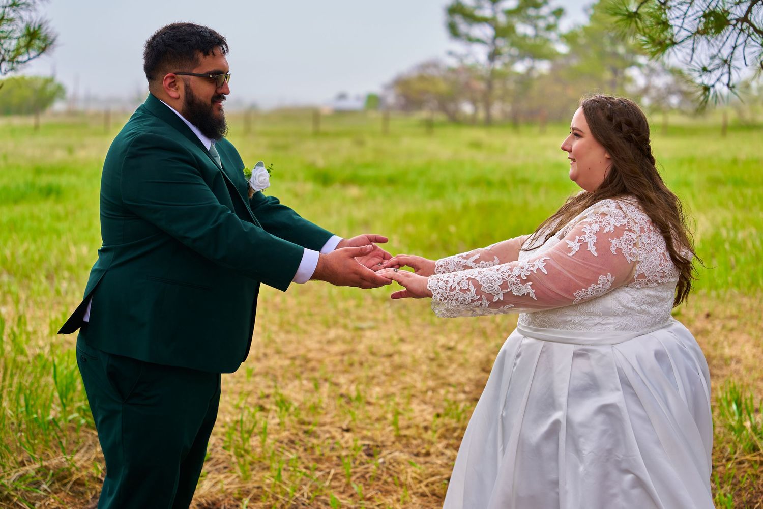 Two people in wedding attire hold hands while standing in a grassy field on their special day.