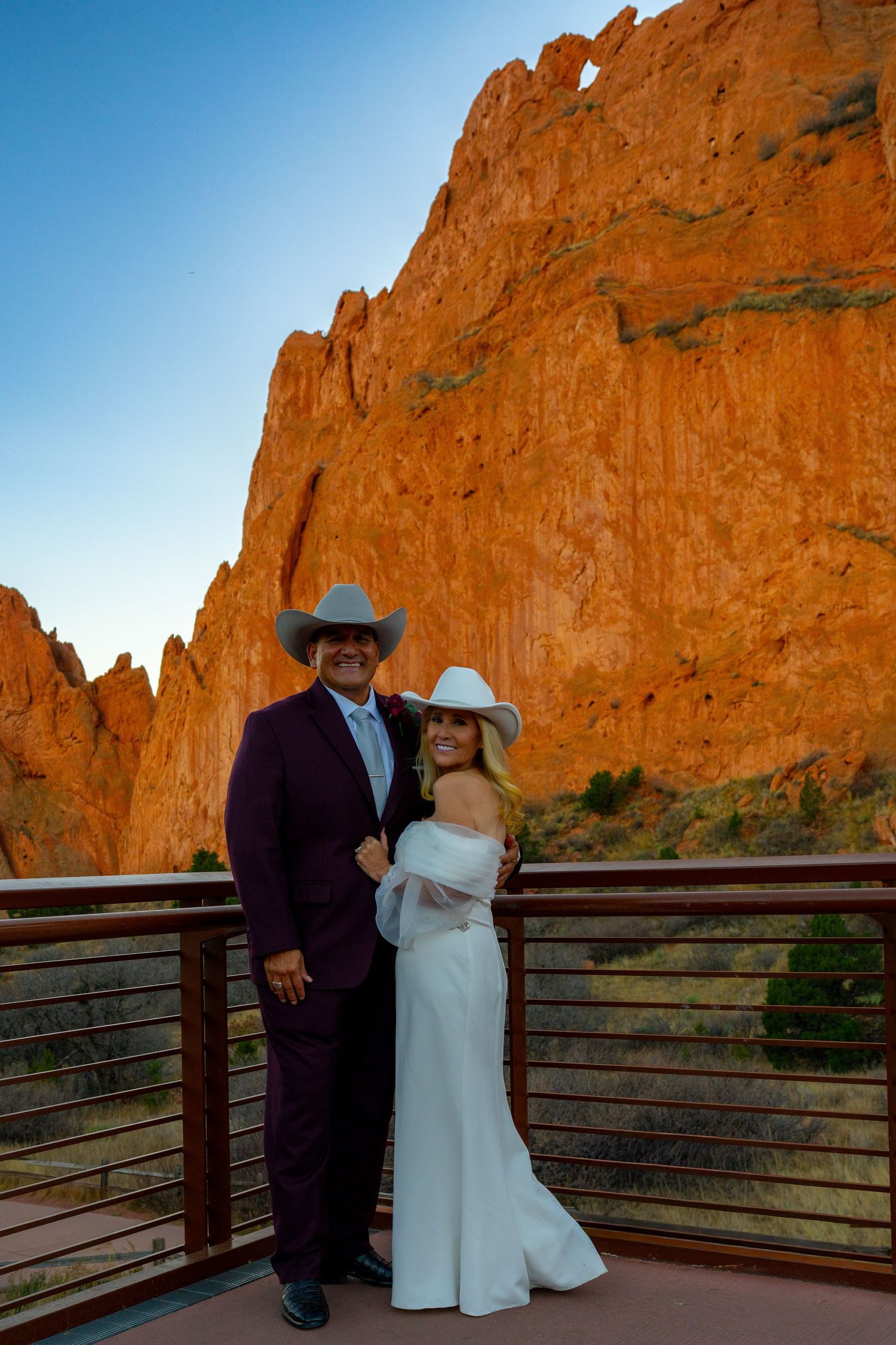 A couple poses on a wooden viewing deck against dramatic red rock cliffs at Garden of the Gods during sunset.