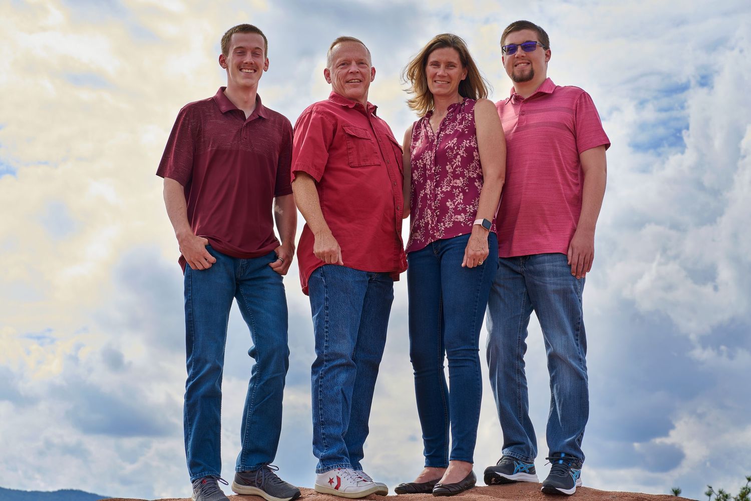 Family of four poses together on rocky overlook against cloudy sky.