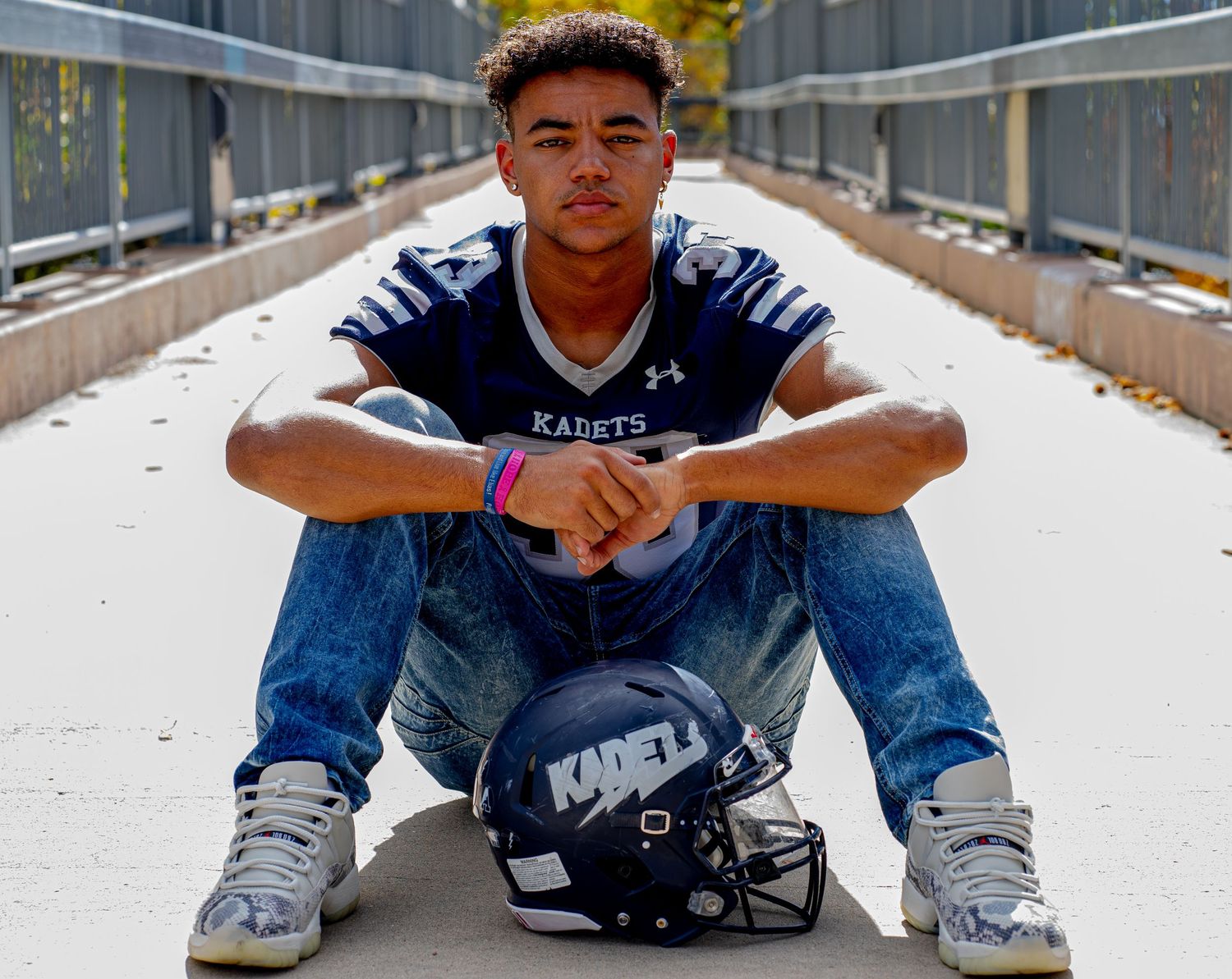 Football player in Kadets uniform sits on walkway with helmet.