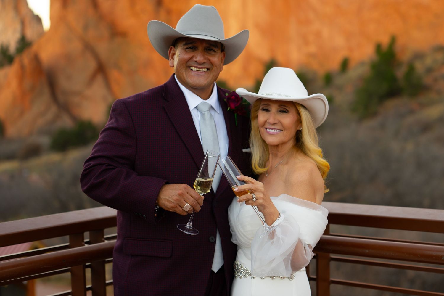 A couple poses together outdoors against red rock formations in formal wedding attire.