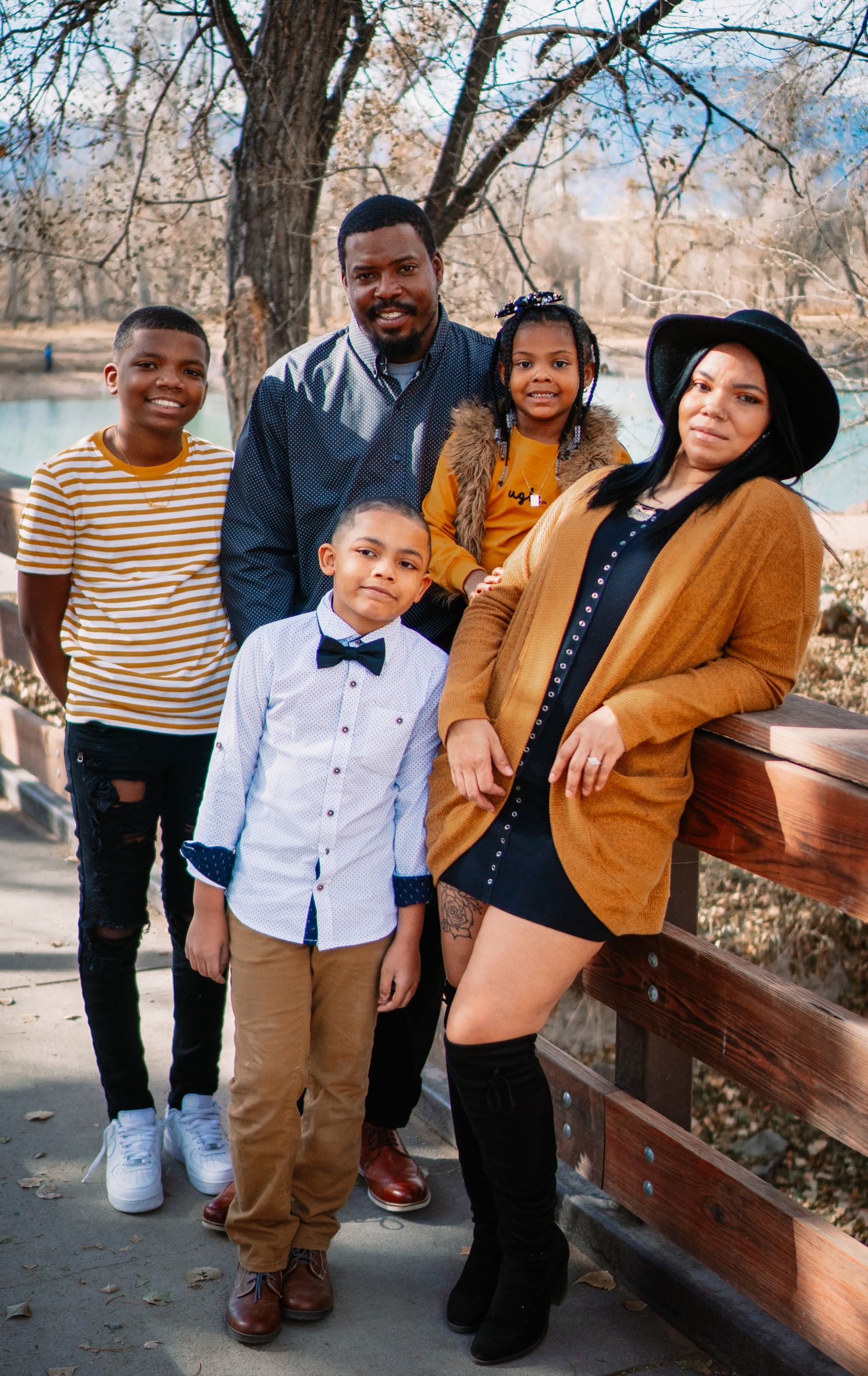 A stylishly dressed family poses together on a wooden bench in a park during autumn.