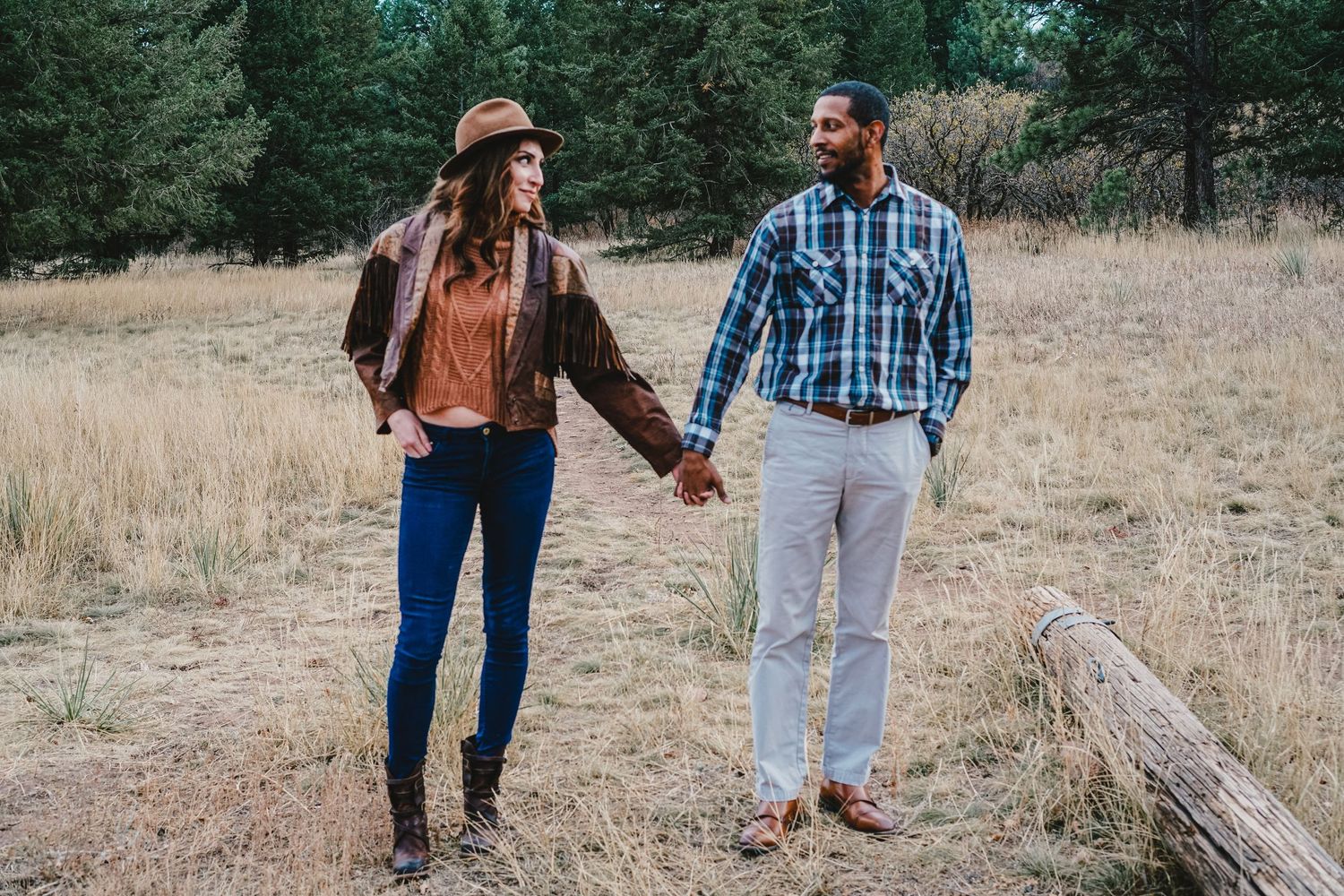 Couple holding hands while walking through mountain meadow in casual attire.