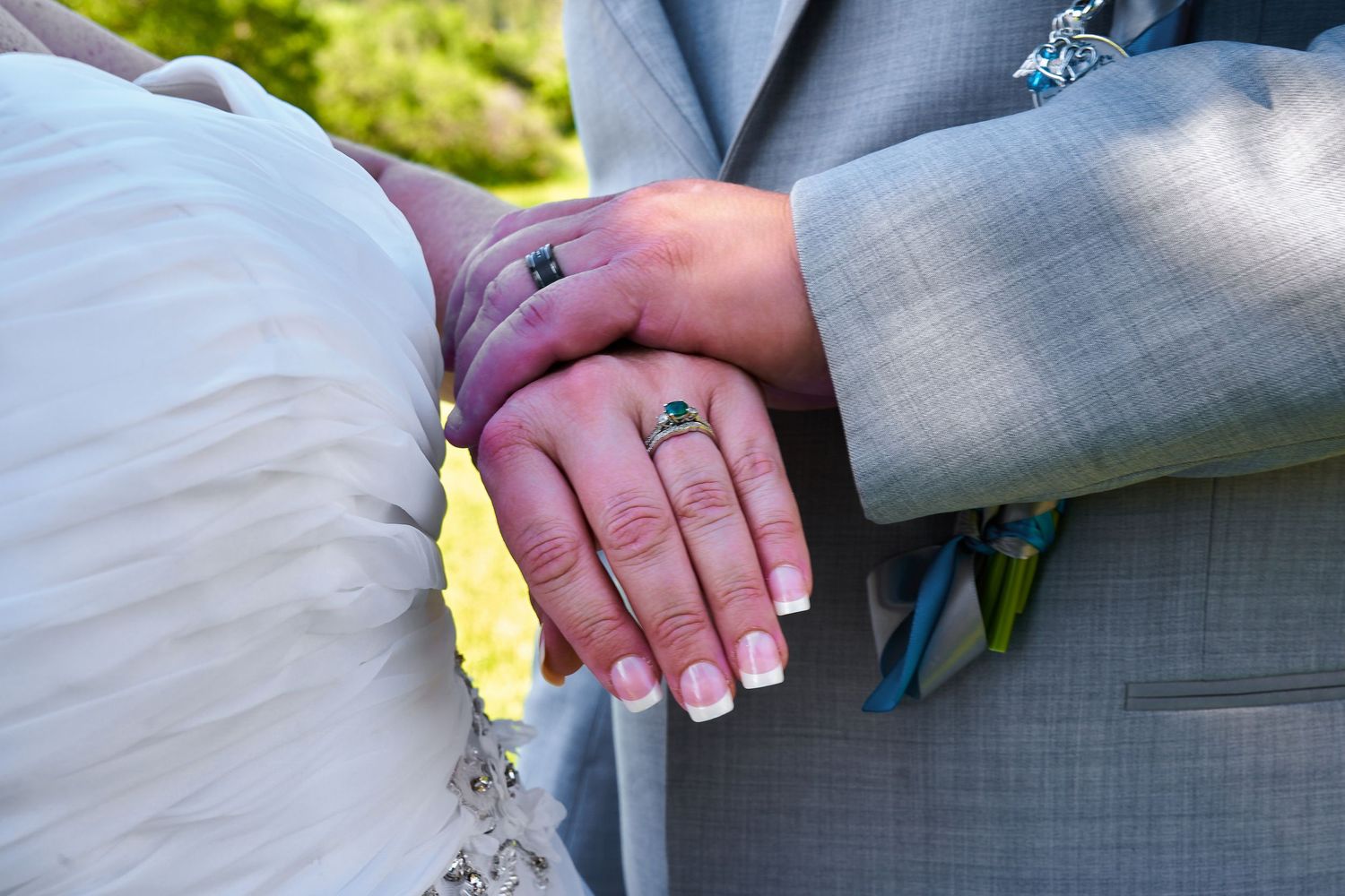 Close-up of wedding rings on joined hands in formal attire.