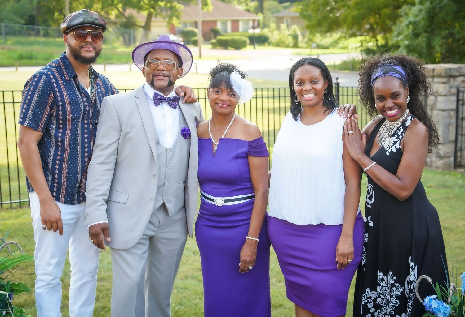A group poses together in formal attire featuring purple and white colors at an outdoor gathering.