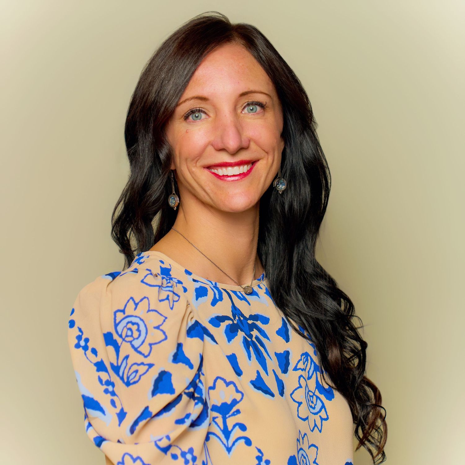 Portrait of woman in blue floral dress with long dark hair against neutral background.