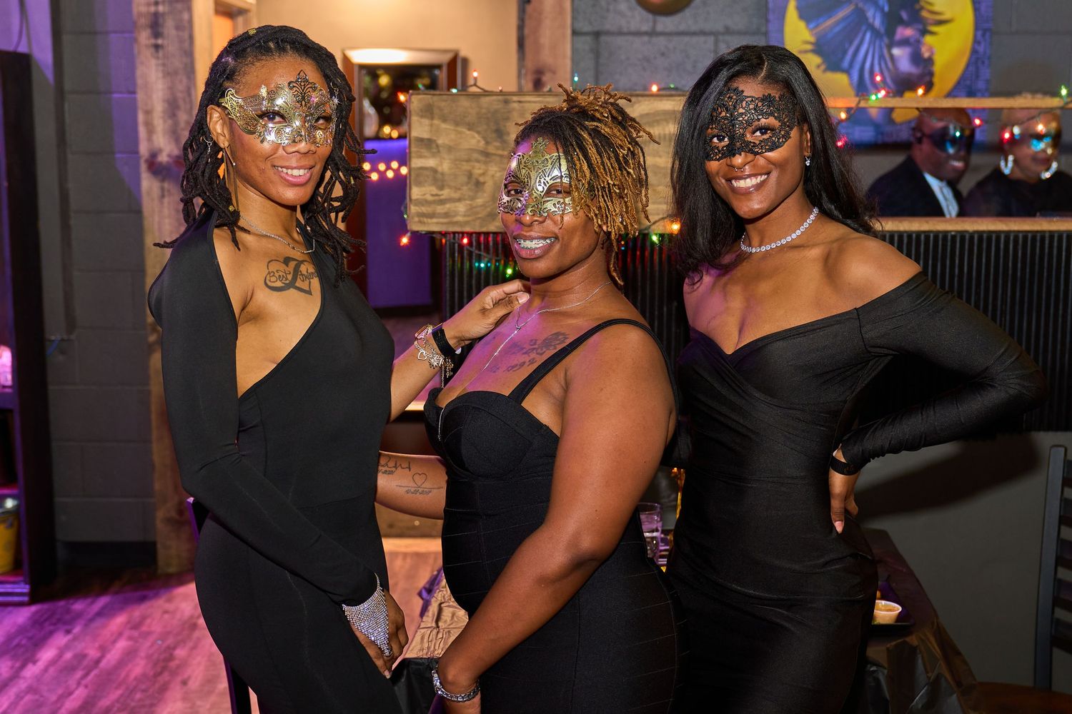 A group of people in black attire dancing and socializing at a party with purple lighting in the background.