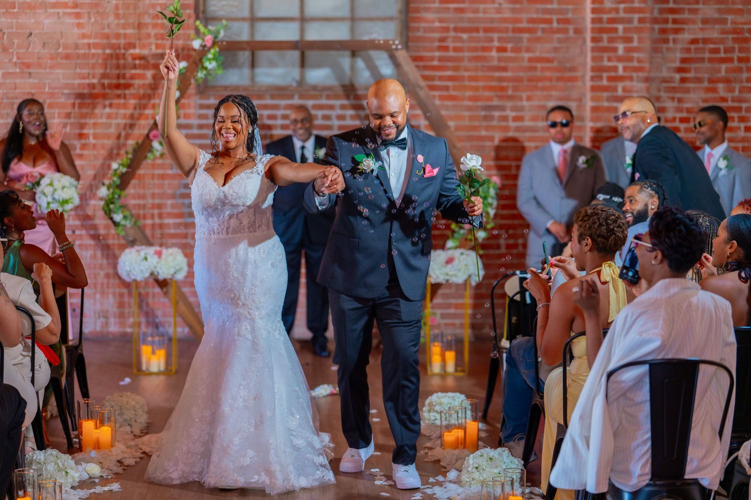 Joyful newlyweds celebrate their wedding ceremony exit in a brick venue, surrounded by cheering guests.