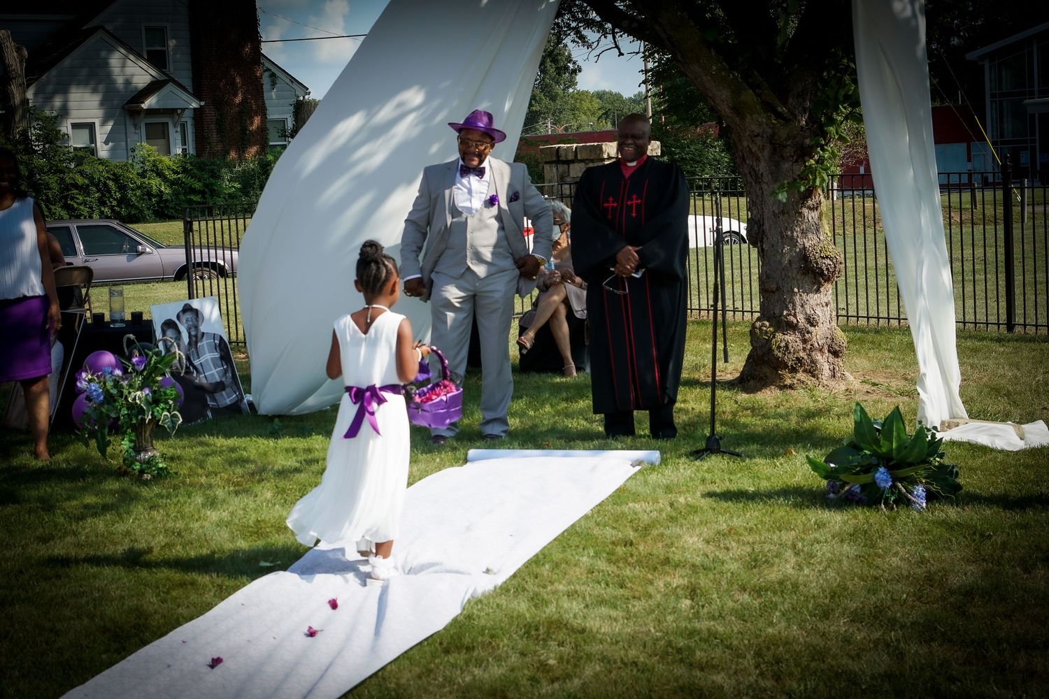 A wedding ceremony procession on a white aisle runner in an outdoor garden setting.