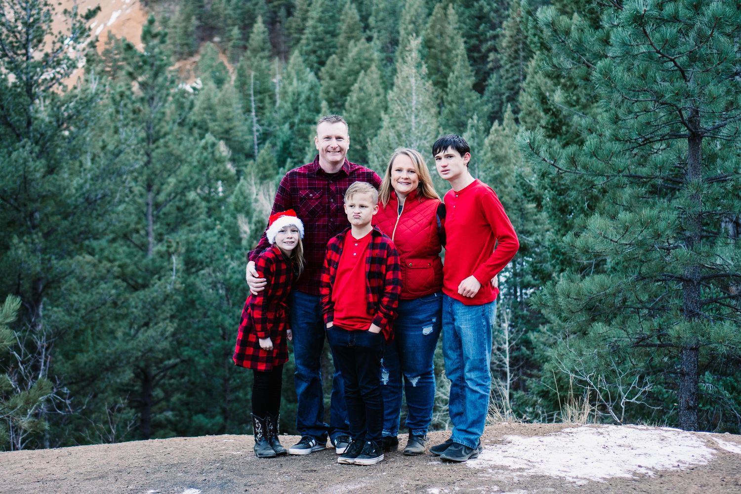 A group in matching red outfits poses together against a backdrop of evergreen trees in the mountains.