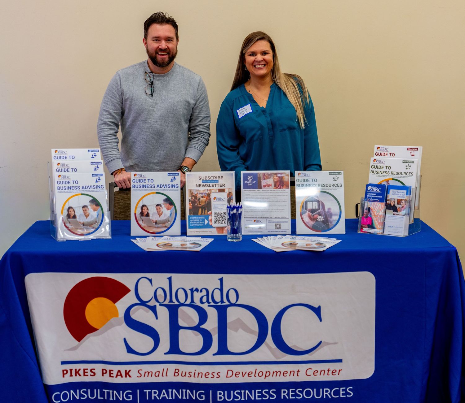 Two representatives stand behind a Colorado SBDC Pikes Peak Small Business Development Center table with brochures.