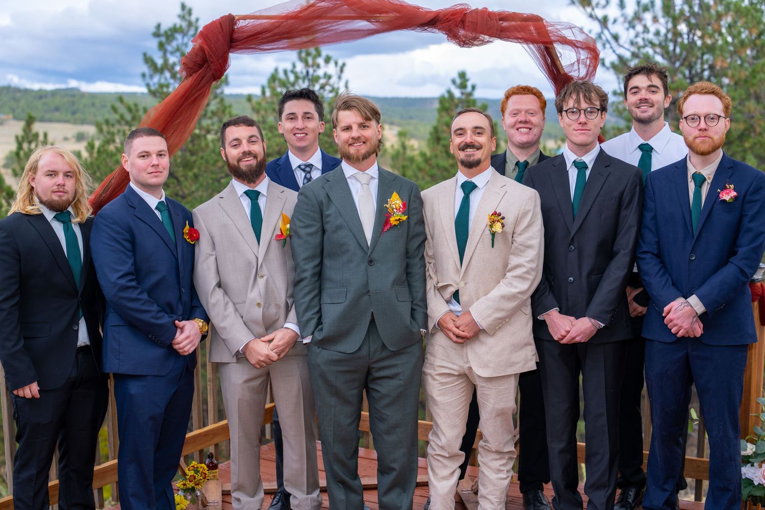 A group wearing suits and formal attire stands together outdoors at a wedding ceremony.