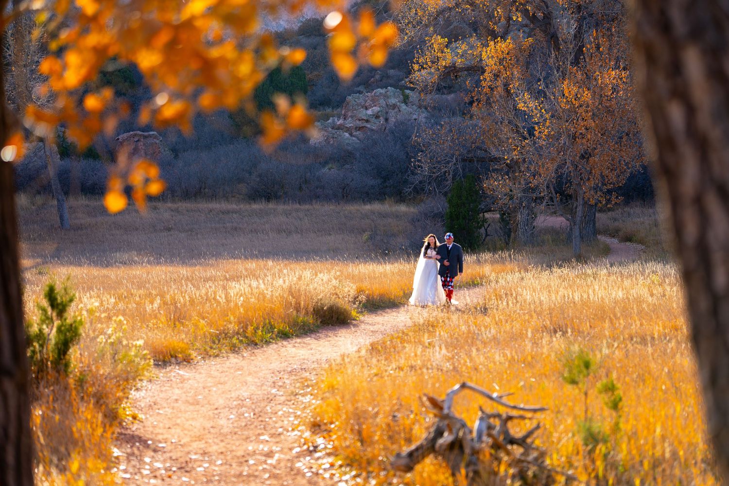 A couple walks along a golden autumn path with orange fall foliage overhead in a park setting.