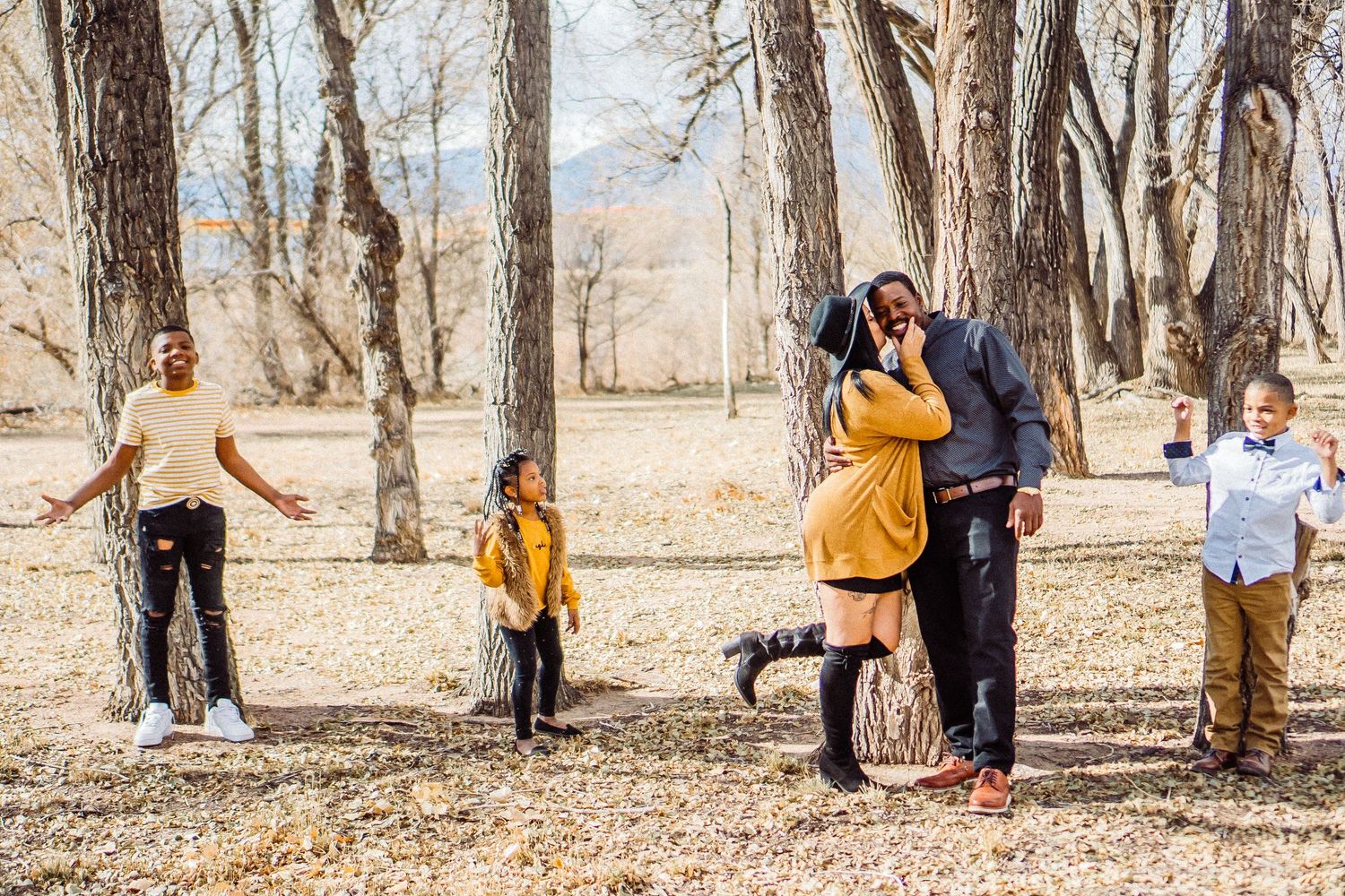 A playful family photo session in a wooded park with fallen leaves.