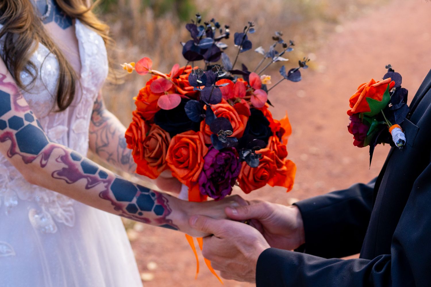 Elegant wedding party holds vibrant red rose and blue hydrangea bouquets while walking outdoors at sunset.