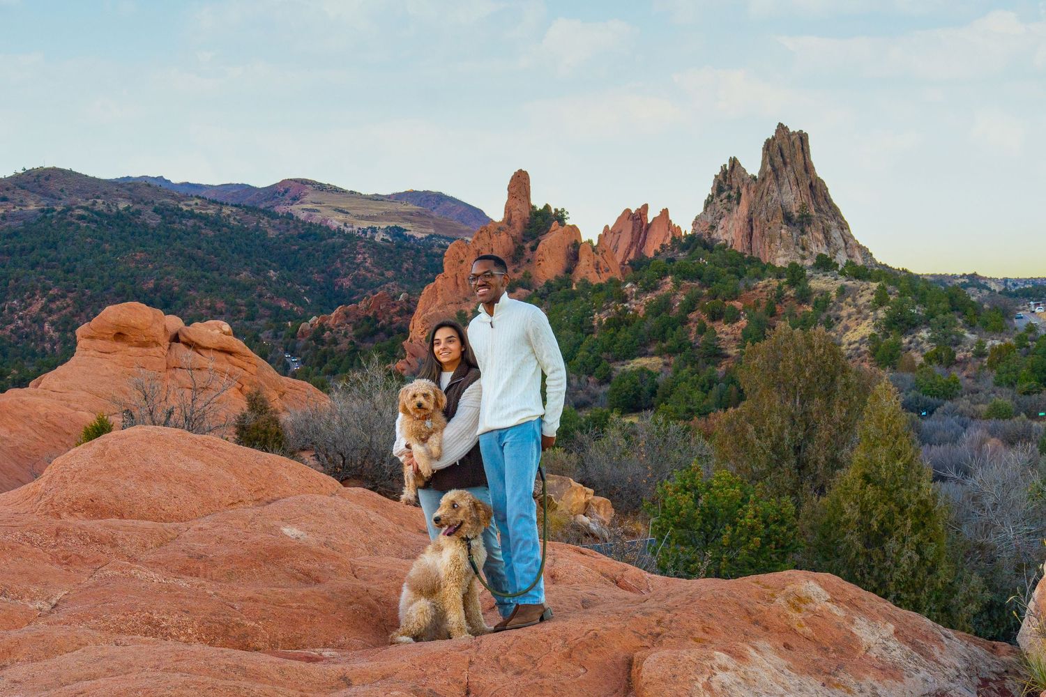 A hiker stands on red sandstone formations overlooking Garden of the Gods park in Colorado during sunset.