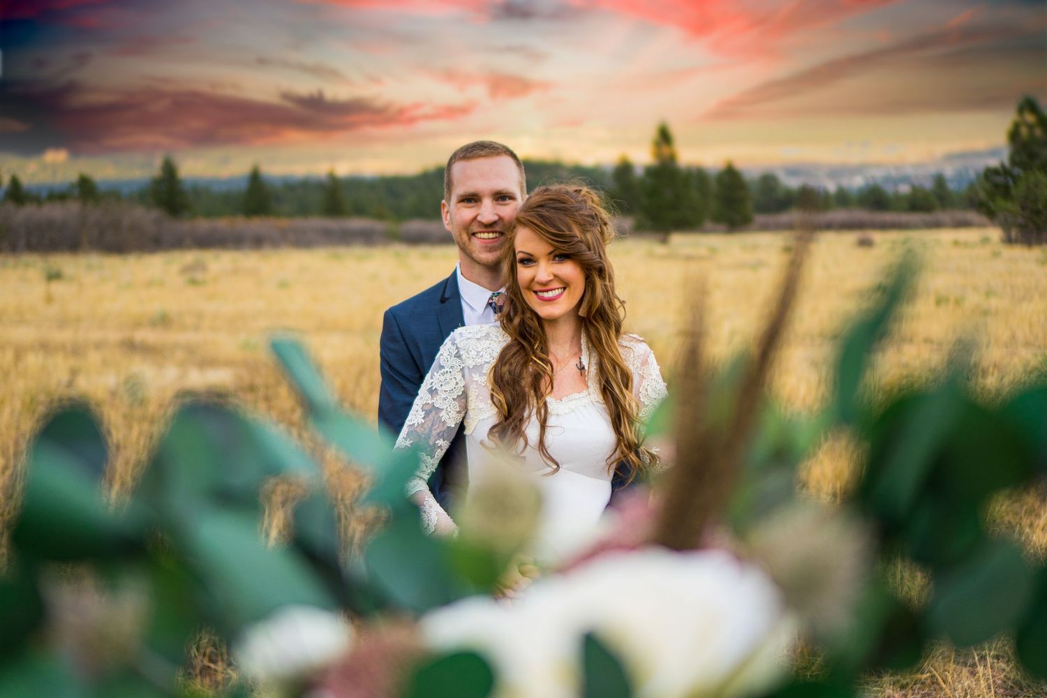 Couple embracing in field during sunset with cactus in foreground.