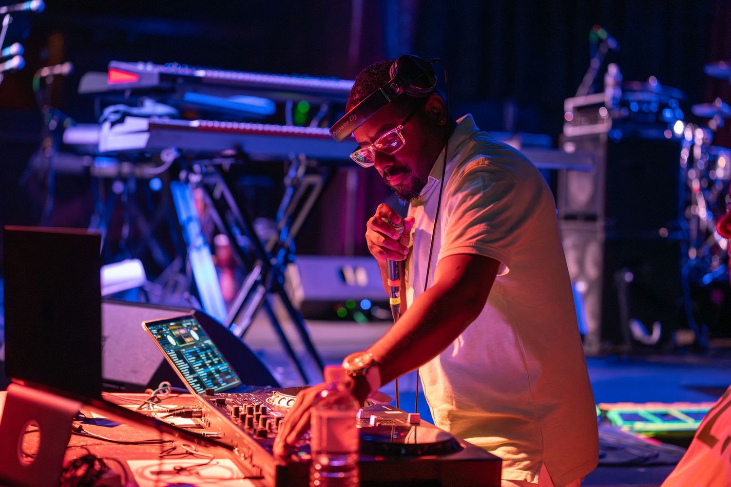 DJ performs at a nightclub with colorful red and blue lighting while operating electronic music equipment.