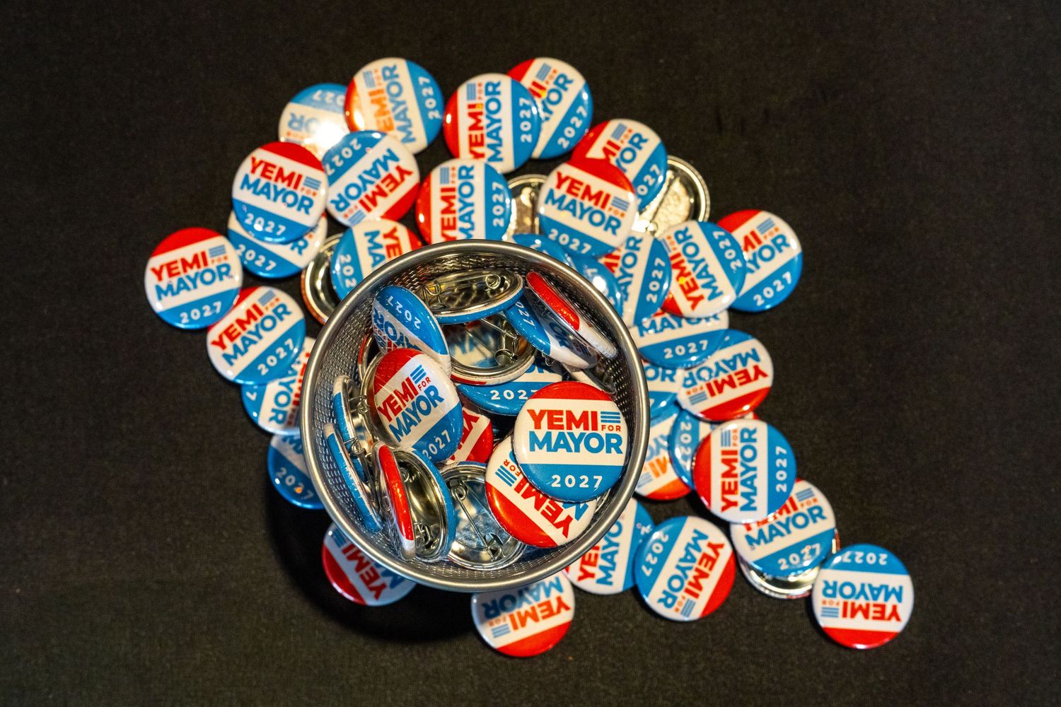 Collection of Yemi for Mayor 2021 campaign buttons arranged in a circle on a dark background.