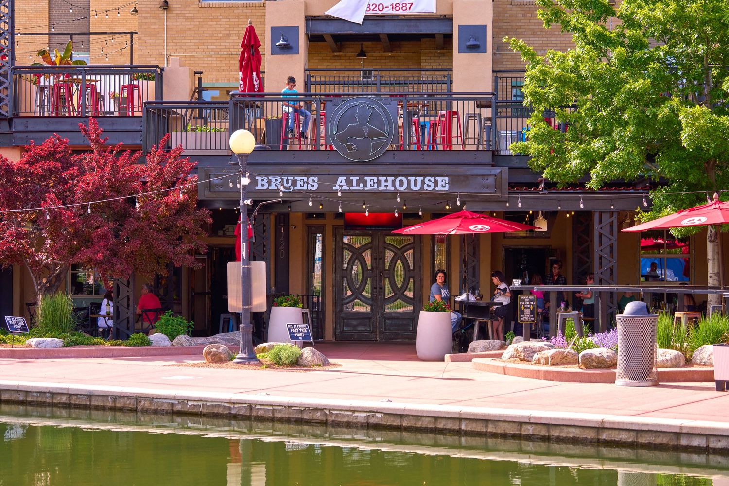 Alehouse restaurant exterior with red umbrellas and waterfront dining area.