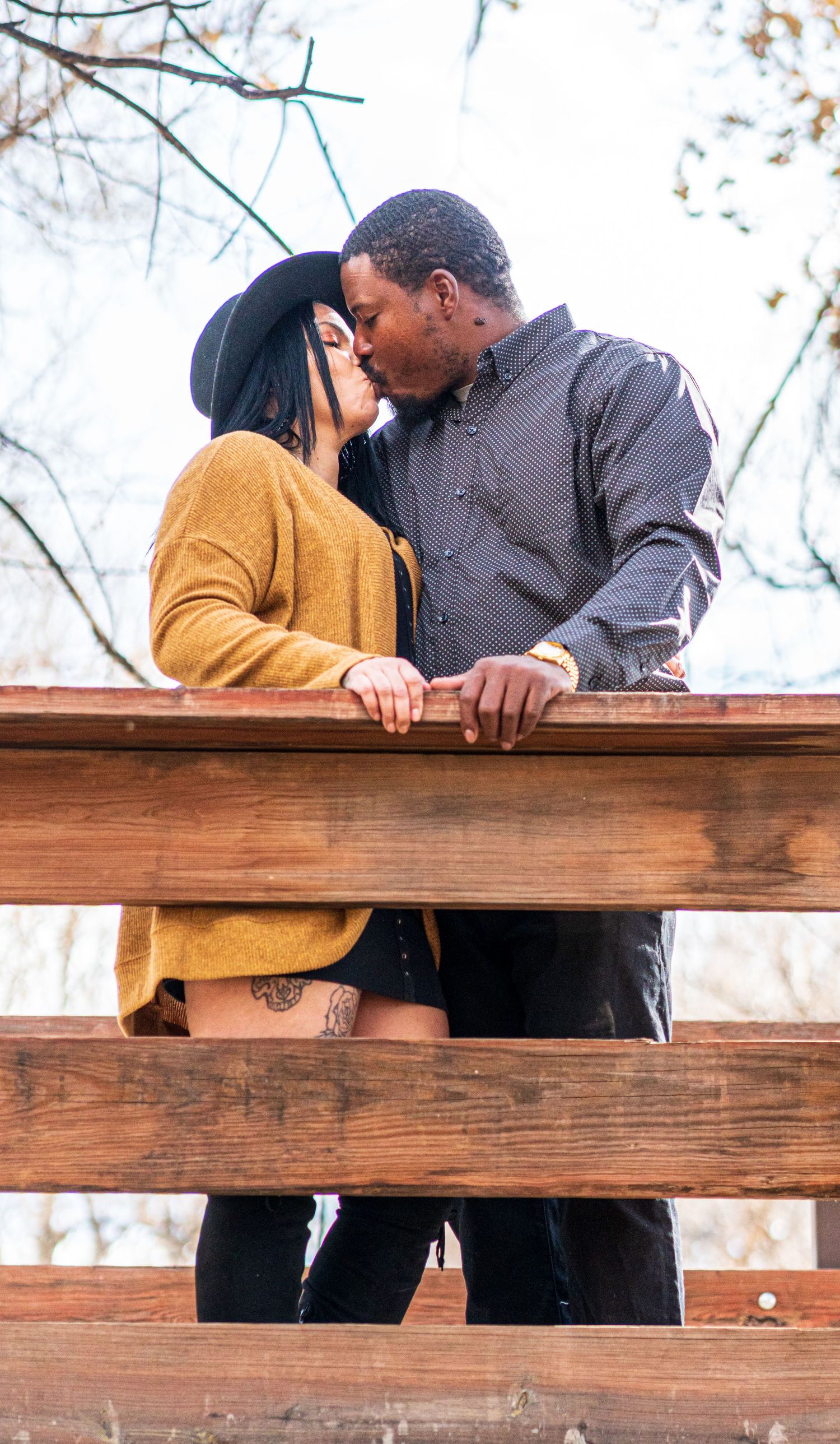 A romantic couple sharing an intimate moment on a wooden bridge in nature.