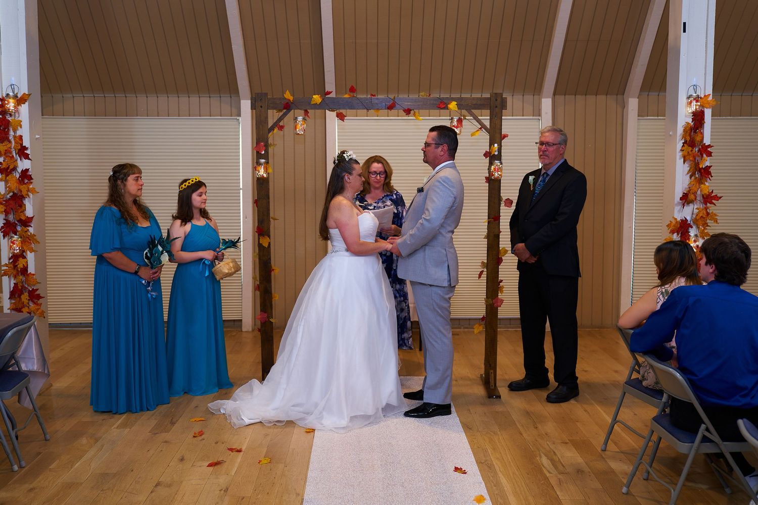 Indoor wedding ceremony under wooden arch with blue-dressed bridesmaids.