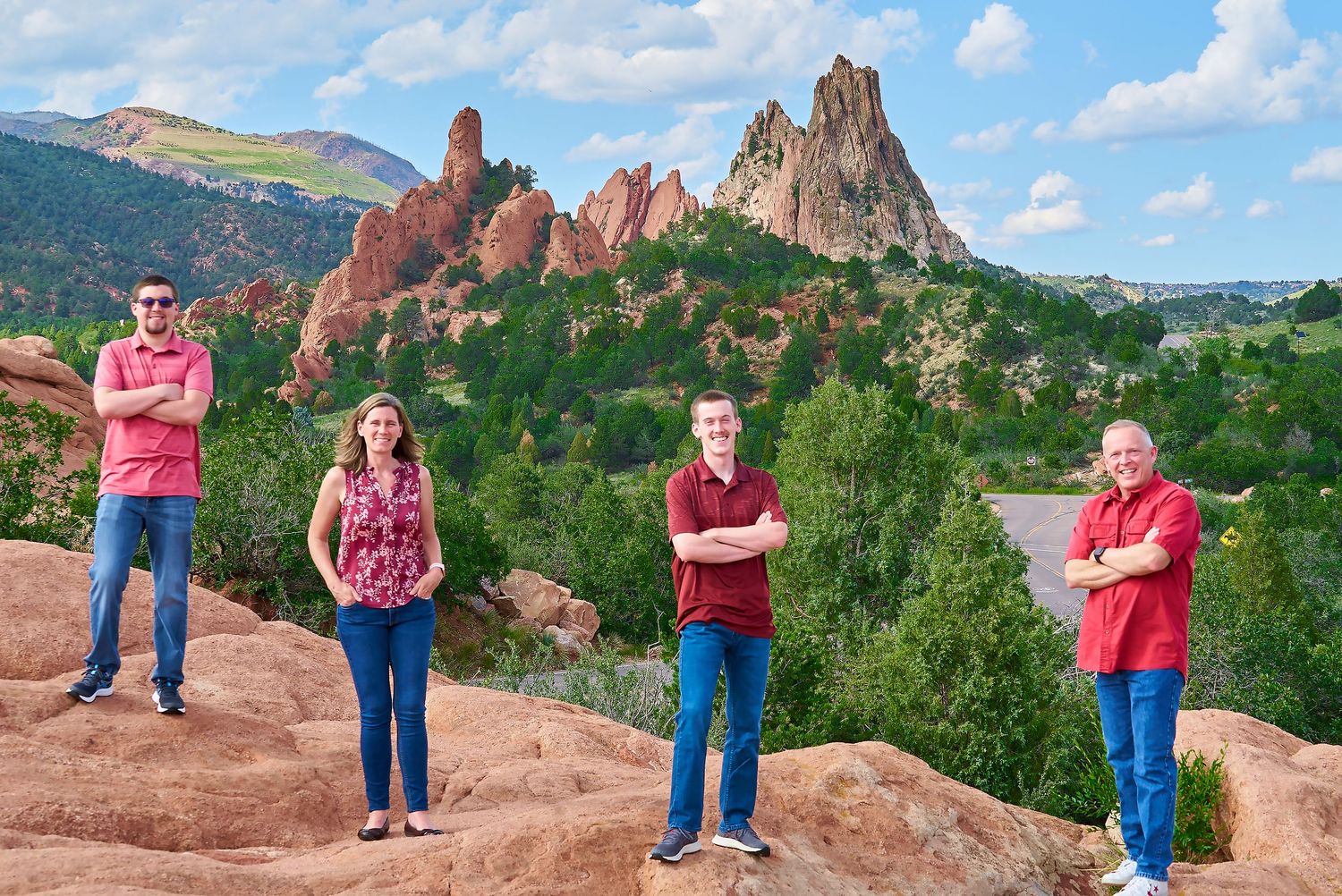 Four people stand spaced apart on red rocks with Garden of the Gods rock formations in background.