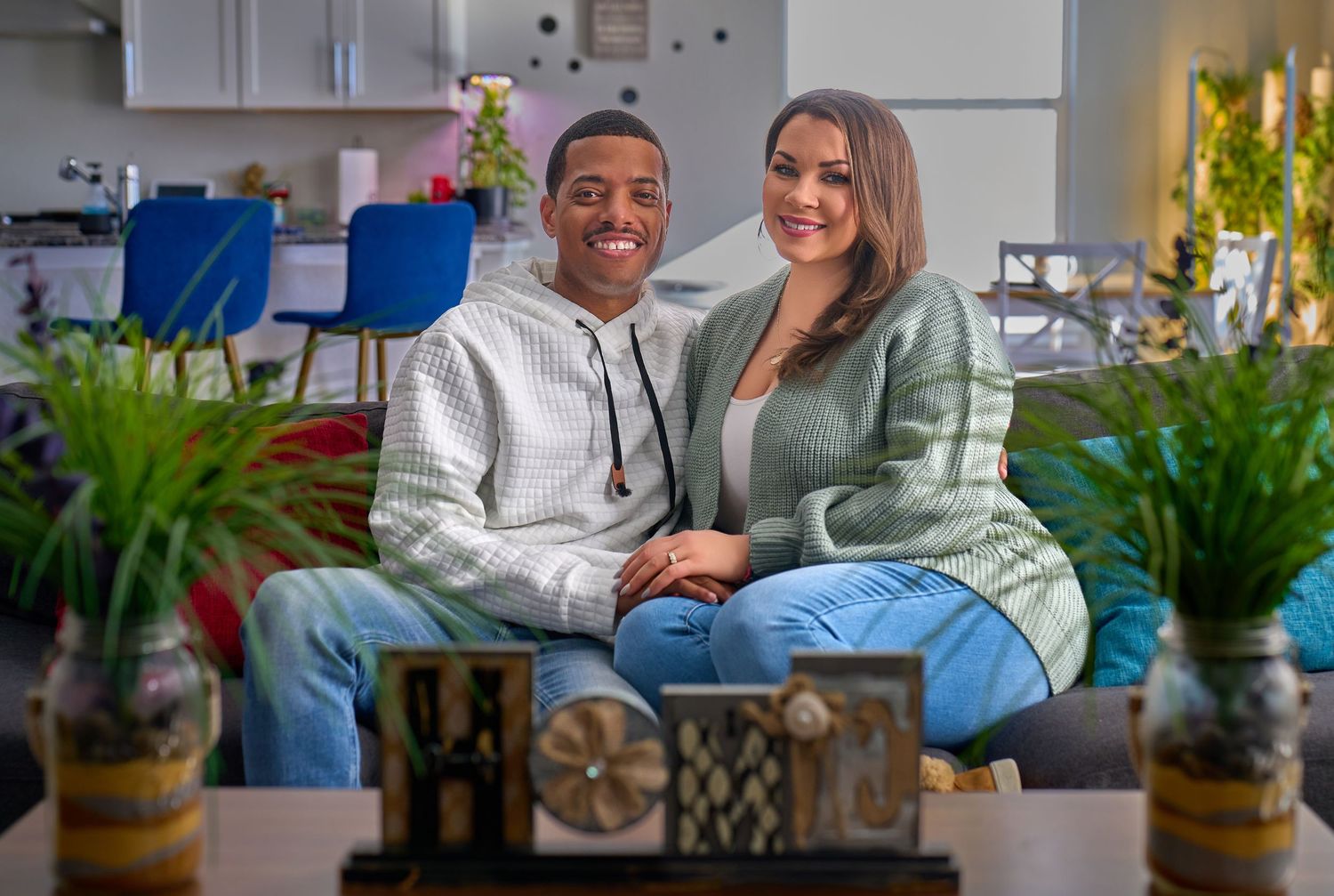 A couple sits together on a couch in a living room decorated with plants and decorative accessories.