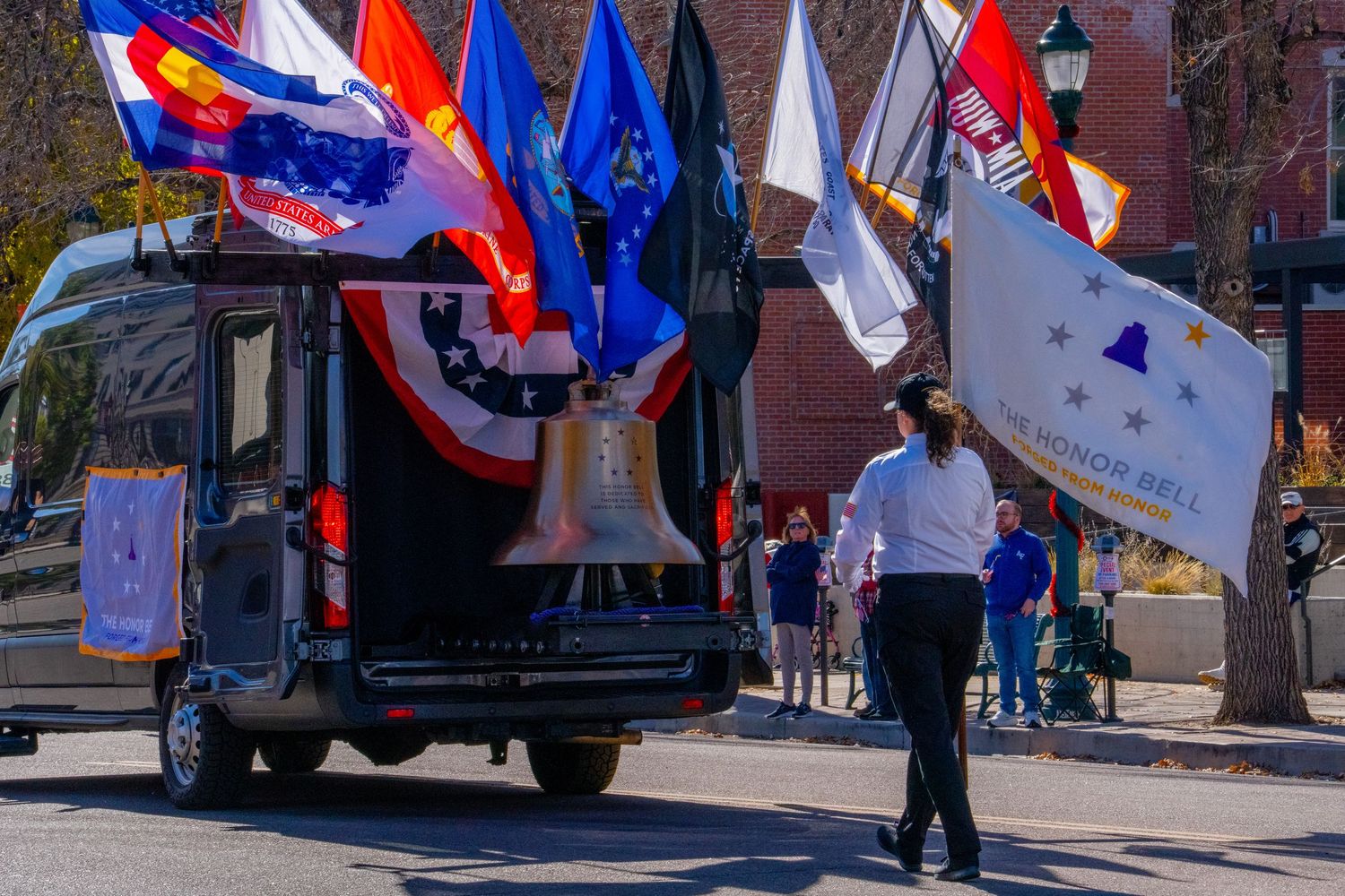 Red, white and blue flags wave during a patriotic parade as people gather along a city street.