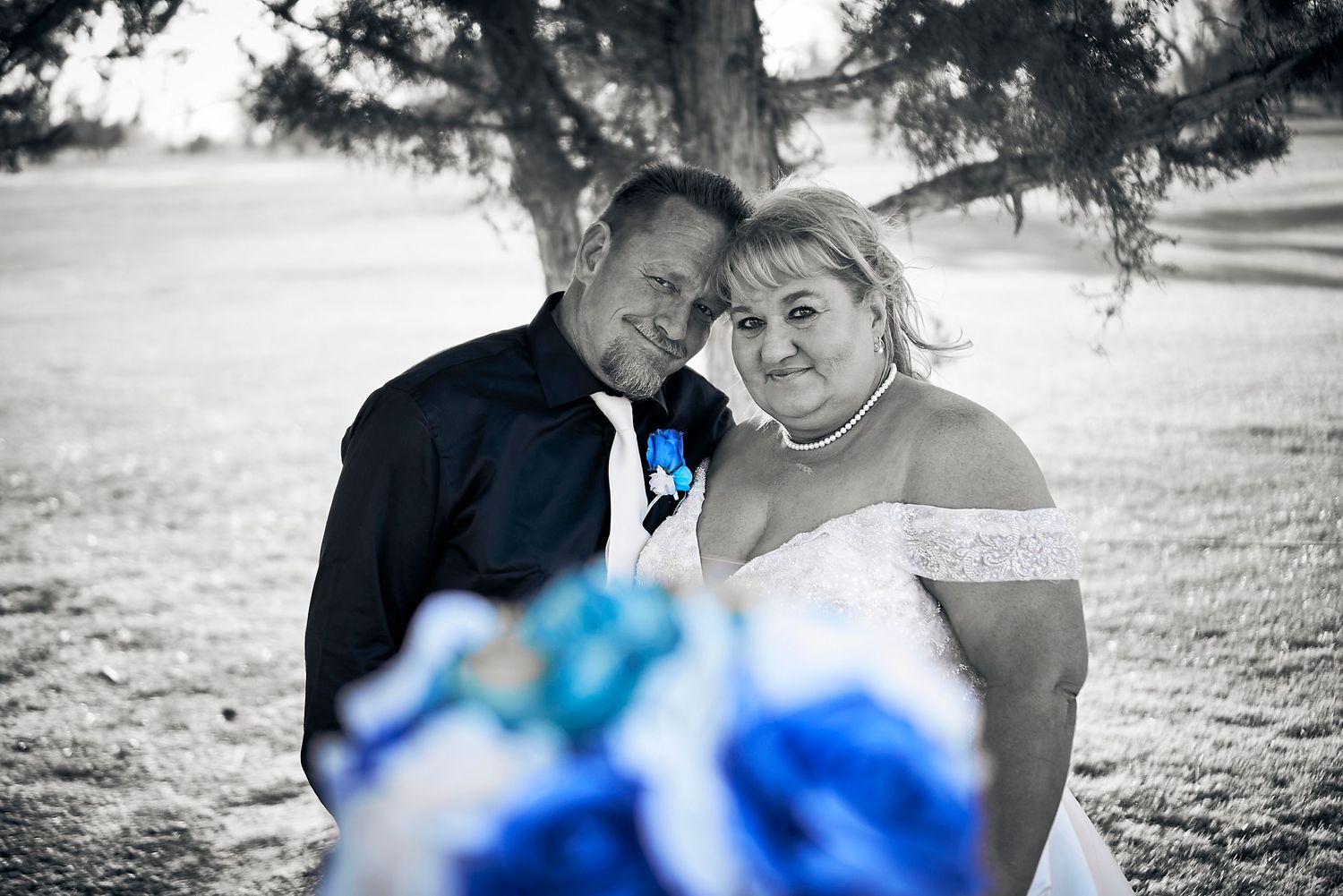 Black and white wedding portrait with blue bouquet accent.
