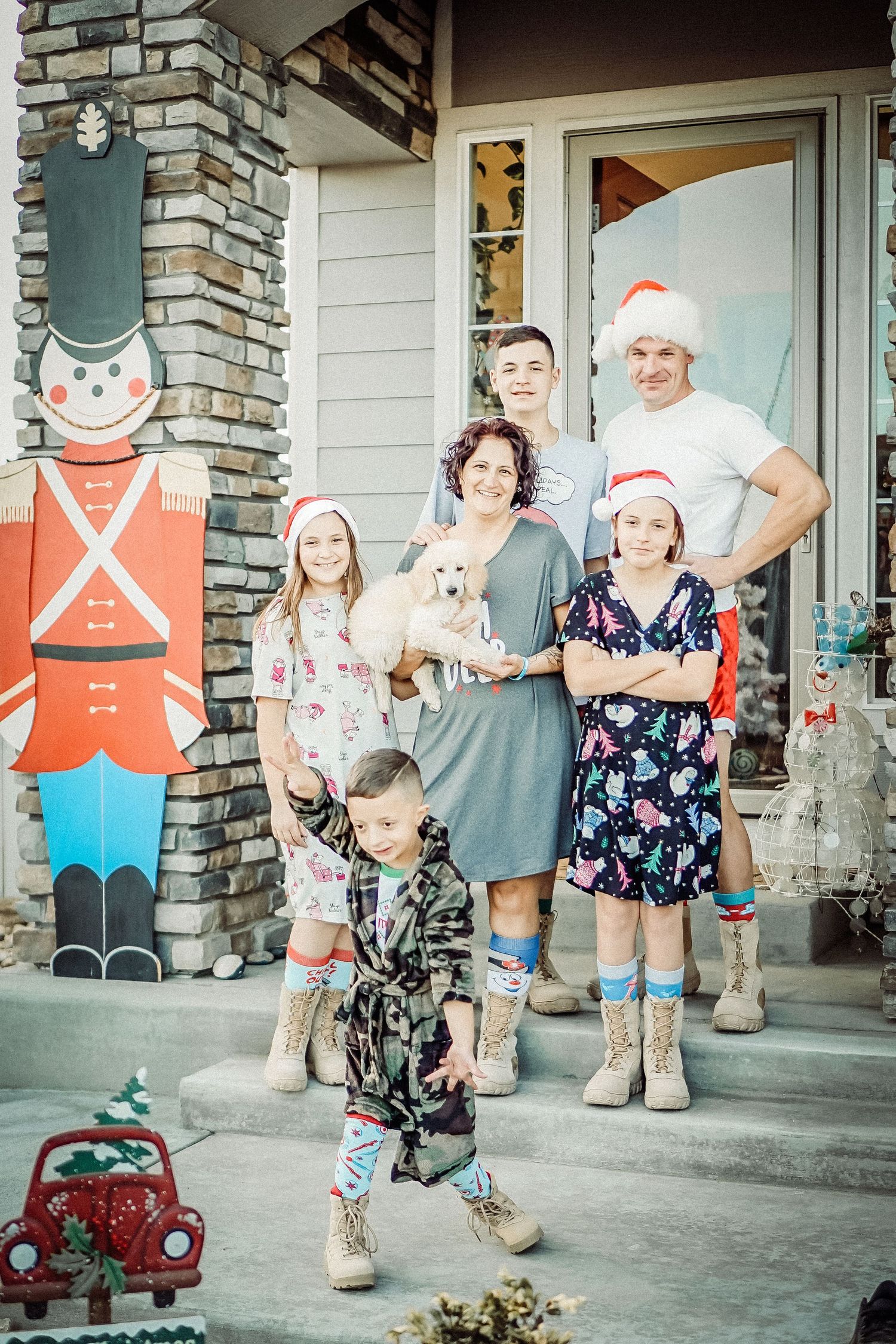 Family posing on front porch with toy nutcracker decoration and small white dog during holidays.