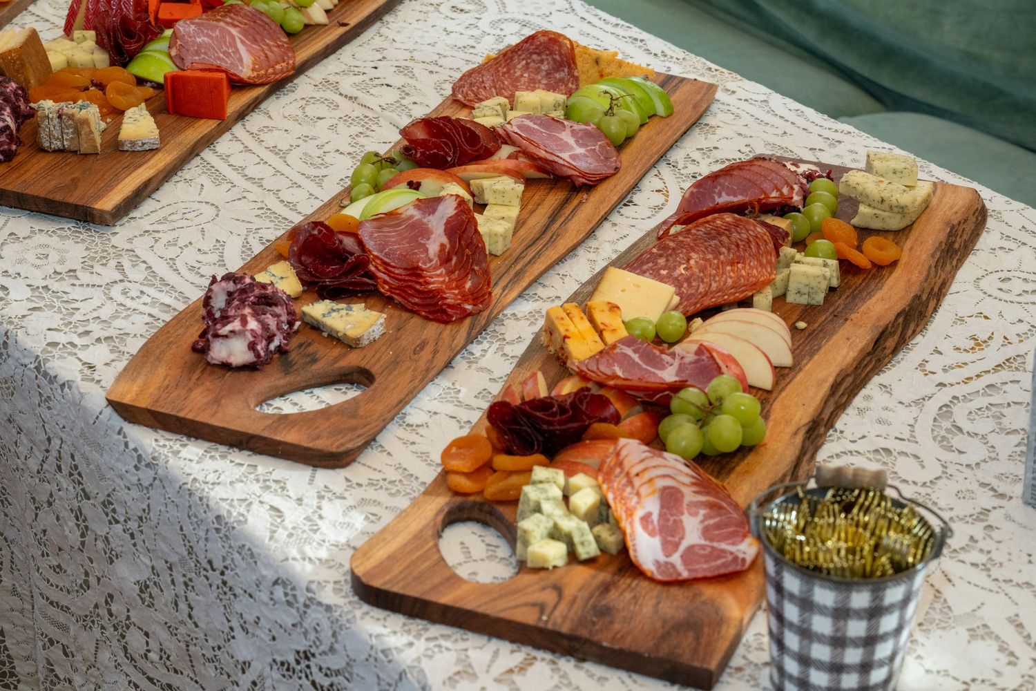 Wooden charcuterie boards topped with meats, cheeses, fruits and other appetizers arranged on a patterned tablecloth.