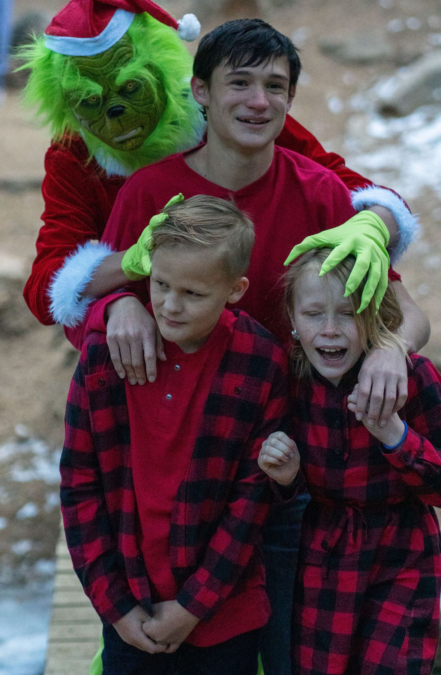Person in Grinch costume posing with children wearing matching red and black plaid flannel shirts.