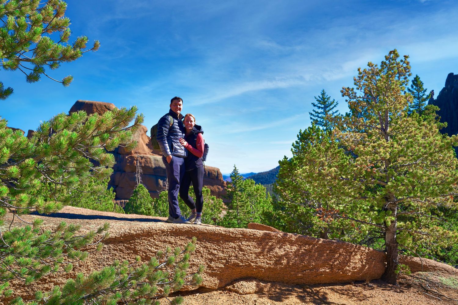 Couple standing on mountain ledge during outdoor proposal.